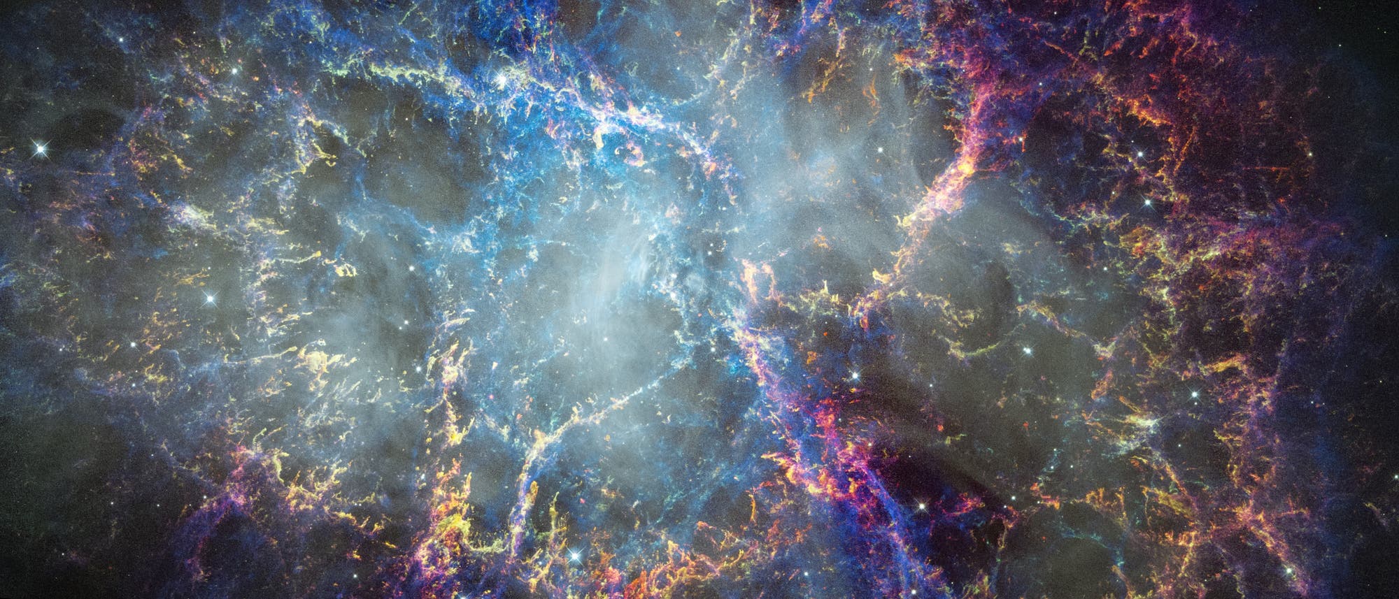 Eine farbenfrohe astronomische Aufnahme des Krebsnebels, die komplexe Strukturen aus leuchtendem Gas und Staub zeigt. Die Farben reichen von Blau &uuml;ber Violett bis zu Orange und Rot, was auf verschiedene chemische Elemente und Temperaturen hinweist. Der Nebel erstreckt sich &uuml;ber das Bild und hebt die dynamische Natur und die Sch&ouml;nheit des Universums hervor. Im Hintergrund sind zahlreiche Sterne zu sehen.