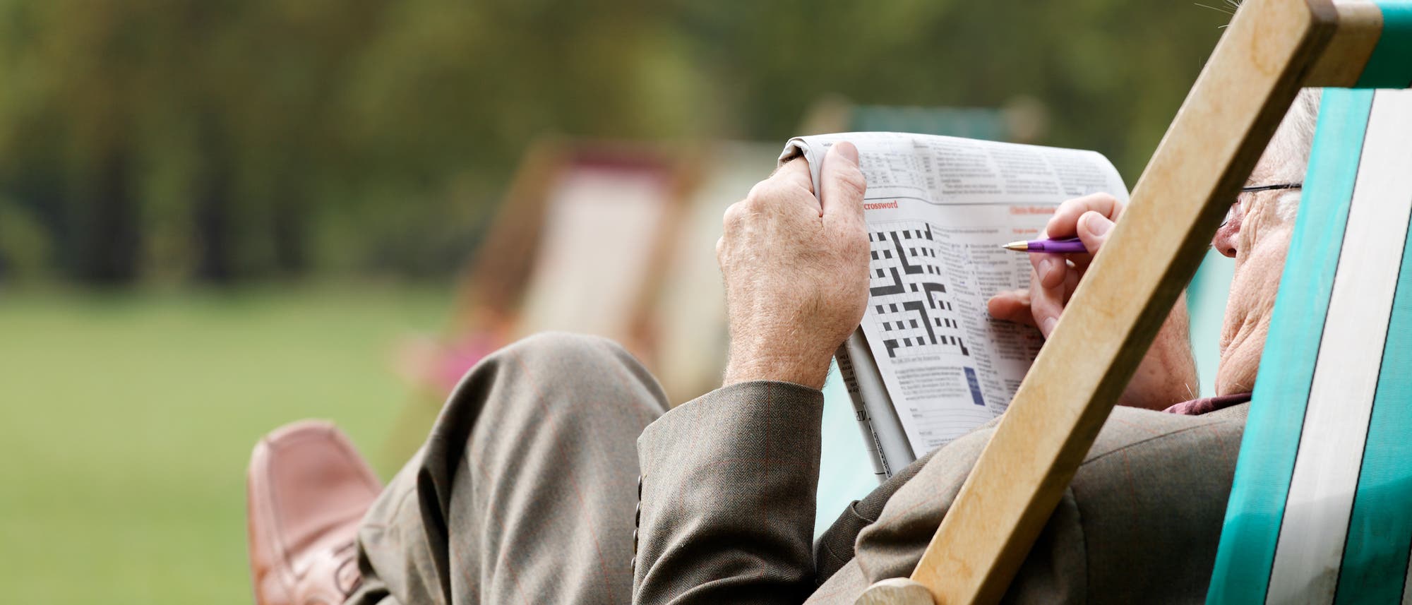Älterer Mann löst Kreuzworträtsel im Gartenstuhl