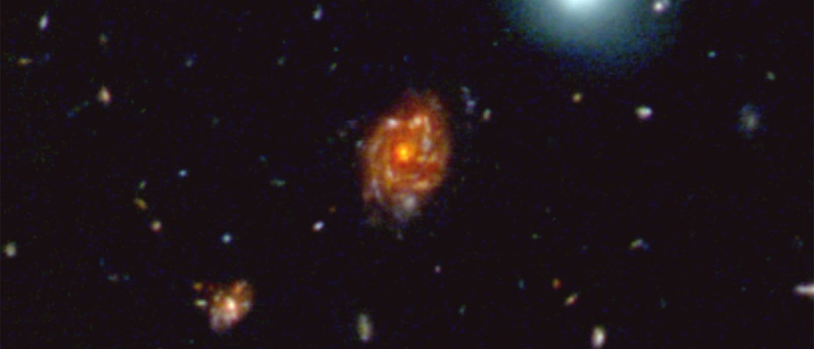 Ein Bild des Weltraums mit mehreren Galaxien. Im Zentrum befindet sich eine leuchtend rote Spiralgalaxie, umgeben von kleineren, blasseren Galaxien. Oben rechts ist eine große, bläulich leuchtende Galaxie zu sehen. Der Hintergrund ist schwarz mit verstreuten Lichtpunkten, die entfernte Sterne oder Galaxien darstellen. Ein Bild des Weltraums mit mehreren Galaxien. Im Zentrum befindet sich eine leuchtend rote Spiralgalaxie, umgeben von kleineren, blasseren Galaxien. Oben rechts ist eine große, bläulich leuchtende Galaxie zu sehen. Der Hintergrund ist schwarz mit verstreuten Lichtpunkten, die entfernte Sterne oder Galaxien darstellen.