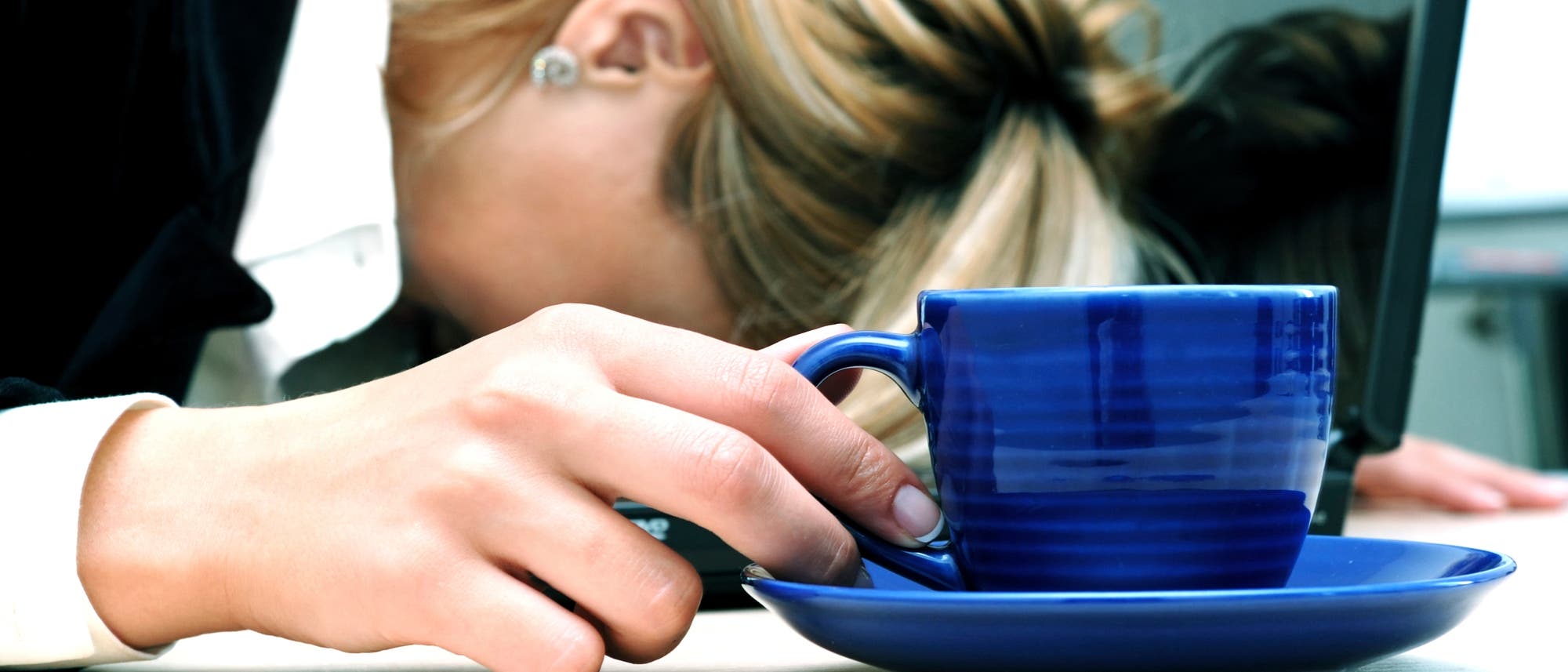 Frau sinkt trotz Kaffee auf ihrem Notebook zusammen