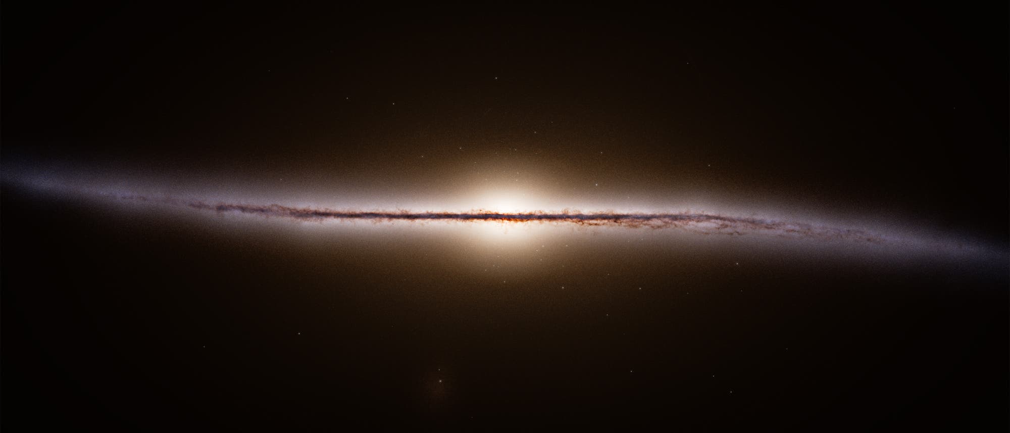 Eine astronomische Aufnahme zeigt eine Galaxie in Kantenansicht. Die Galaxie erscheint als dünner, leuchtender Streifen mit einem hellen Zentrum, umgeben von einem dunklen Hintergrund. Feine Details der Staub- und Gasstrukturen sind entlang des Streifens sichtbar. Im Hintergrund sind vereinzelte Sterne zu erkennen. Eine astronomische Aufnahme zeigt eine Galaxie in Kantenansicht. Die Galaxie erscheint als dünner, leuchtender Streifen mit einem hellen Zentrum, umgeben von einem dunklen Hintergrund. Feine Details der Staub- und Gasstrukturen sind entlang des Streifens sichtbar. Im Hintergrund sind vereinzelte Sterne zu erkennen.