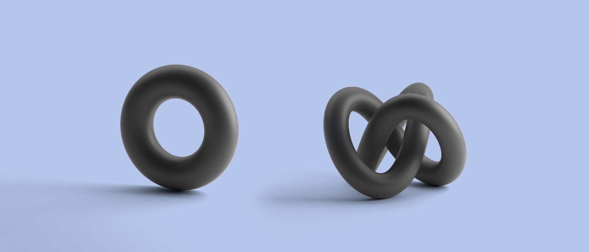 Zwei schwarze, dreidimensionale Formen auf einem hellblauen Hintergrund. Links ist ein einzelner, aufrecht stehender Torus zu sehen. Rechts befinden sich drei ineinander verschlungene Torus-Formen, die eine komplexe, verknotete Struktur bilden. Die Szene vermittelt ein Gefühl von Balance und Kontrast zwischen Einfachheit und Komplexität. Zwei schwarze, dreidimensionale Formen auf einem hellblauen Hintergrund. Links ist ein einzelner, aufrecht stehender Torus zu sehen. Rechts befinden sich drei ineinander verschlungene Torus-Formen, die eine komplexe, verknotete Struktur bilden. Die Szene vermittelt ein Gefühl von Balance und Kontrast zwischen Einfachheit und Komplexität.