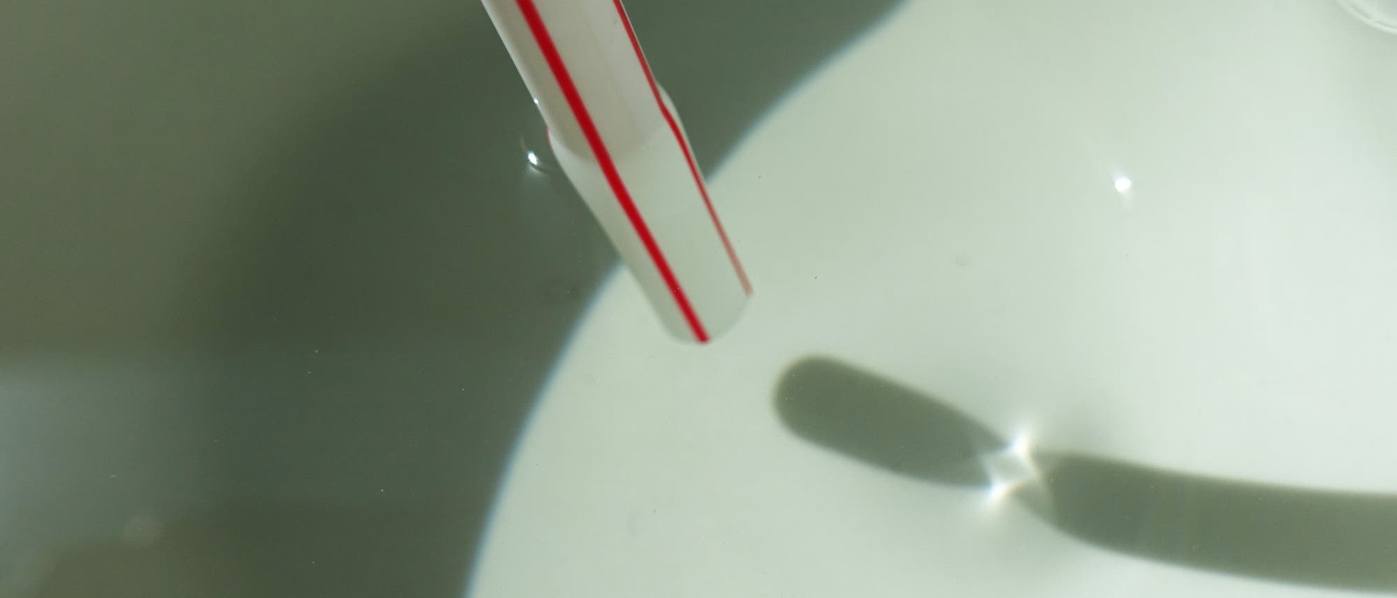 Der Schatten eines Strohhalms auf dem Boden eines Behälters zerfällt in zwei Teile. Sie sind durch eine charakteristische Kaustik getrennt.