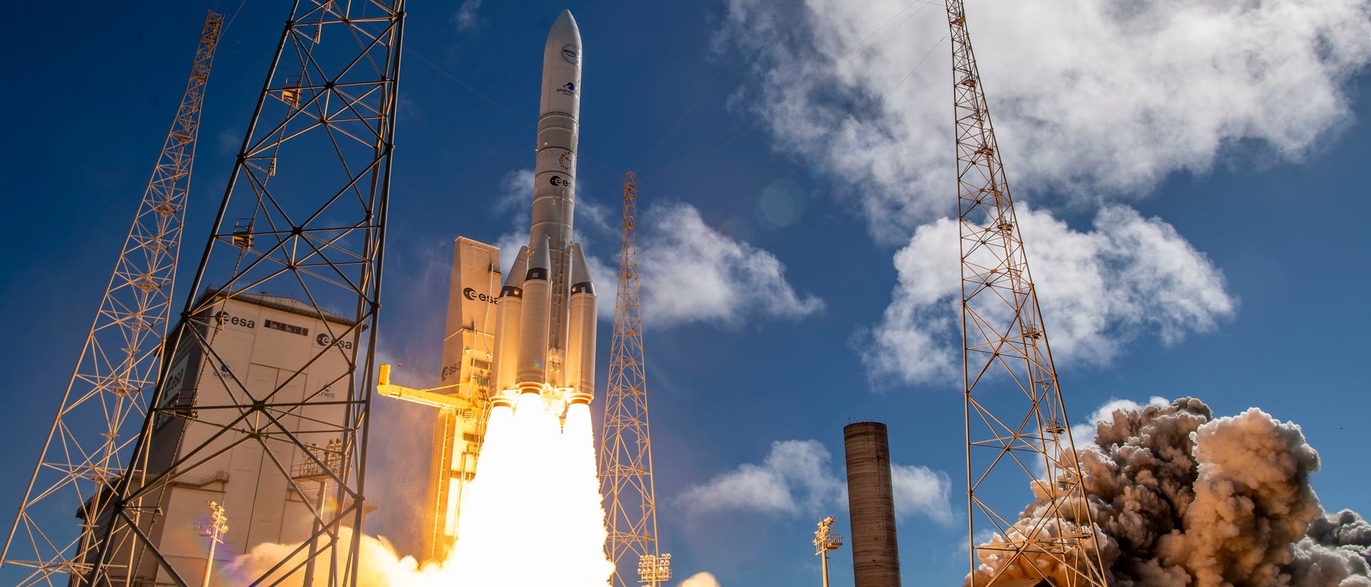 Eine Rakete hebt von einer Startrampe ab, umgeben von Rauch und Flammen. Der Himmel ist klar mit einigen Wolken. Auf der Rakete und der Startrampe sind Logos der ESA zu sehen. Im Hintergrund sind hohe Metallstrukturen sichtbar. Eine Rakete hebt von einer Startrampe ab, umgeben von Rauch und Flammen. Der Himmel ist klar mit einigen Wolken. Auf der Rakete und der Startrampe sind Logos der ESA zu sehen. Im Hintergrund sind hohe Metallstrukturen sichtbar.
