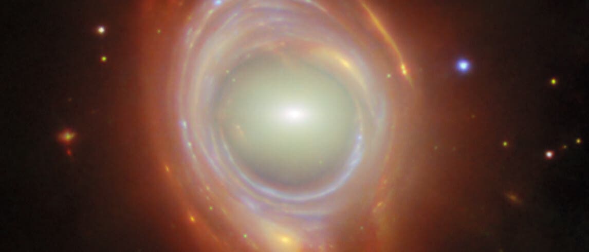 Ein faszinierendes Bild einer Galaxie mit einem hellen, leuchtenden Zentrum, umgeben von spiralförmigen, rötlichen Gas- und Staubwolken. Die Struktur ähnelt einem kosmischen Wirbel, der von zahlreichen kleinen, funkelnden Sternen umgeben ist. Der Hintergrund ist dunkel, was die leuchtenden Farben der Galaxie hervorhebt. Ein faszinierendes Bild einer Galaxie mit einem hellen, leuchtenden Zentrum, umgeben von spiralförmigen, rötlichen Gas- und Staubwolken. Die Struktur ähnelt einem kosmischen Wirbel, der von zahlreichen kleinen, funkelnden Sternen umgeben ist. Der Hintergrund ist dunkel, was die leuchtenden Farben der Galaxie hervorhebt.