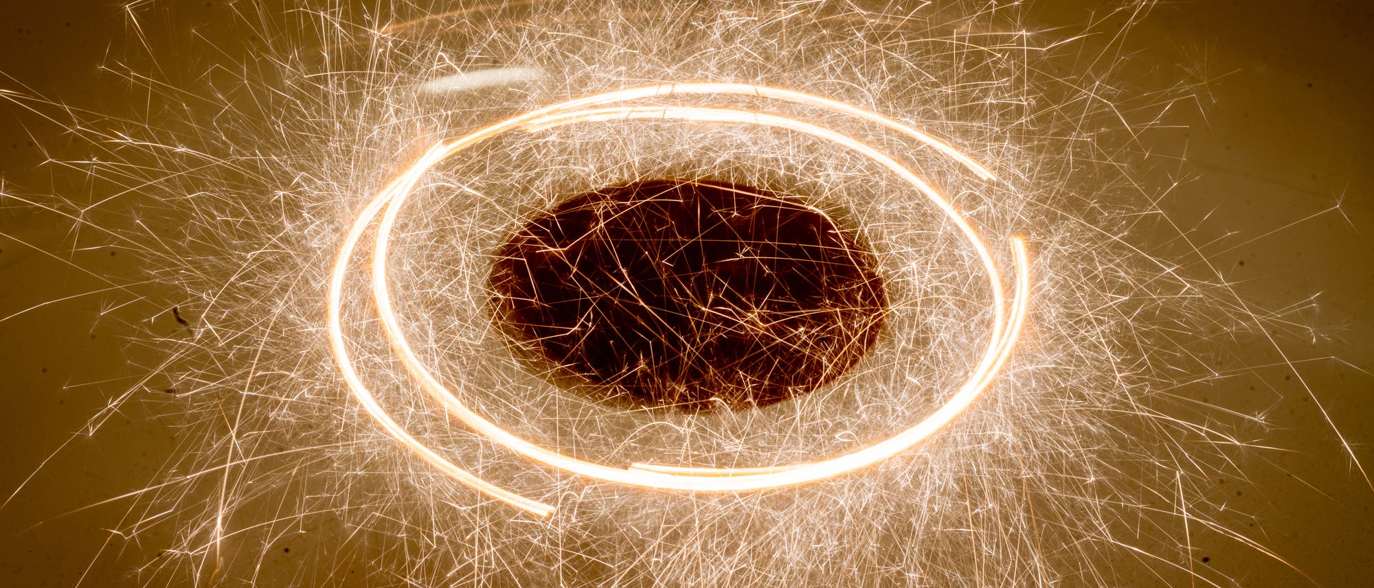 Brennende Wunderkerzen, die tangential an einer Scheibe aufgehängt sind, hinterlassen sprühende Funken, während sich die Scheibe im Kreis dreht. Eine lange Belichtungsdauer macht die glühenden Stäbe als Strichspuren sichtbar. Brennende Wunderkerzen, die tangential an einer Scheibe aufgehängt sind, hinterlassen sprühende Funken, während sich die Scheibe im Kreis dreht. Eine lange Belichtungsdauer macht die glühenden Stäbe als Strichspuren sichtbar.