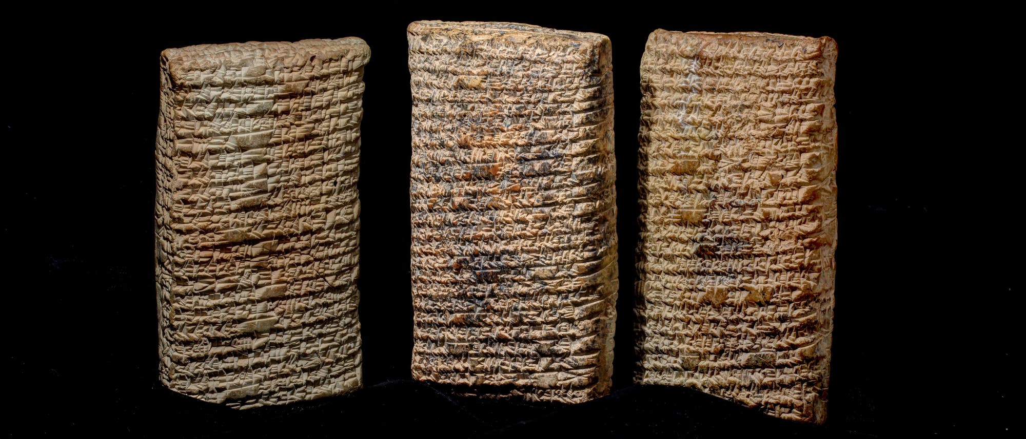 Drei altbabylonische Tontafeln mit Keilschrift, die aufrecht nebeneinander stehen. Die Tafeln sind mit dicht geschriebenen, eingravierten Zeichen bedeckt, die literarische Informationen enthalten. Der Hintergrund ist schwarz, was den Fokus auf die Textur und Details der Tafeln lenkt.