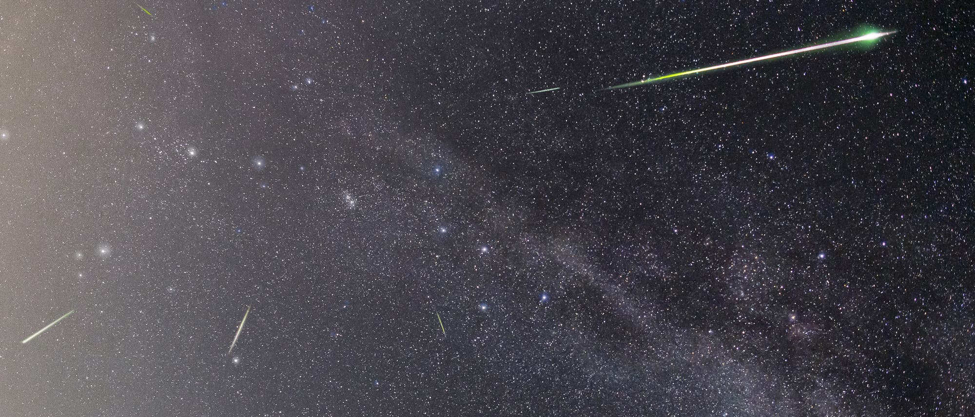 Sternenbedeckter Nachthimmel mit mehreren Meteoren, die als helle, leuchtende Streifen erscheinen. Die Milchstra&szlig;e ist als nebliges Band sichtbar, das sich diagonal &uuml;ber das Bild erstreckt. Die Meteore variieren in Helligkeit und Richtung, was auf einen Meteorstrom hindeutet. Der Himmel ist klar und voller Sterne unterschiedlicher Helligkeit.