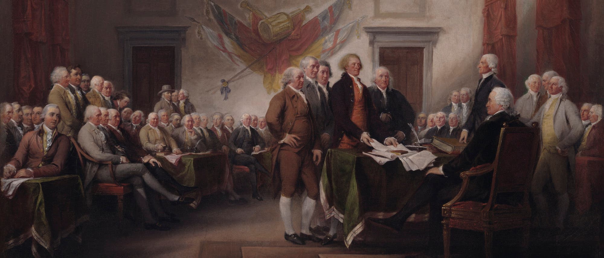  Eine historische Gem&auml;lde-Szene zeigt eine Gruppe von M&auml;nnern in einem gro&szlig;en Raum, die sich um einen Tisch versammelt haben. Einige stehen, w&auml;hrend andere sitzen. Im Hintergrund sind Fahnen und ein gro&szlig;es Symbol an der Wand zu sehen. Die M&auml;nner tragen Kleidung aus dem 18.&nbsp;Jahrhundert. Der Raum ist mit roten Vorh&auml;ngen und Holzvert&auml;felungen dekoriert. Die Szene vermittelt den Eindruck einer wichtigen Versammlung oder Unterzeichnung. 
