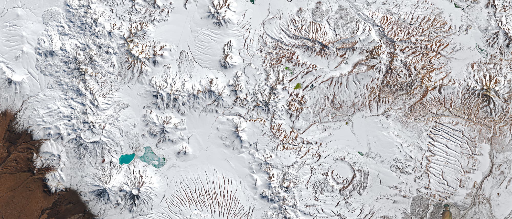 Satellitenbild einer geografischen Karte der Andenregion in S&uuml;damerika, die schneebedeckte Berge und T&auml;ler zeigt. Mehrere gr&uuml;ne und t&uuml;rkisfarbene Seen sind sichtbar. Der Schriftzug &bdquo;ALMA&ldquo; markiert die Position des Atacama Large Millimeter/submillimeter Array. Die Karte hebt die kontrastreiche Landschaft zwischen den schneebedeckten Gipfeln und den braunen, trockenen Ebenen hervor.