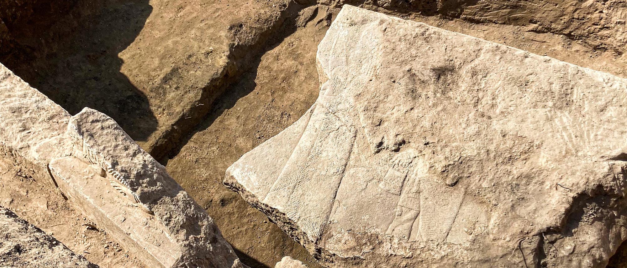 Eine archäologische Ausgrabungsstätte zeigt einen teilweise frei gelegten, großen Steinblock mit eingravierten Linien und Mustern. Der Stein liegt in einer Grube aus Erde und Sand. Die Oberfläche des Steins ist rau und weist Spuren von Verwitterung auf. Die Szene vermittelt den Eindruck von historischer Bedeutung und archäologischer Forschung. Eine archäologische Ausgrabungsstätte zeigt einen teilweise frei gelegten, großen Steinblock mit eingravierten Linien und Mustern. Der Stein liegt in einer Grube aus Erde und Sand. Die Oberfläche des Steins ist rau und weist Spuren von Verwitterung auf. Die Szene vermittelt den Eindruck von historischer Bedeutung und archäologischer Forschung.