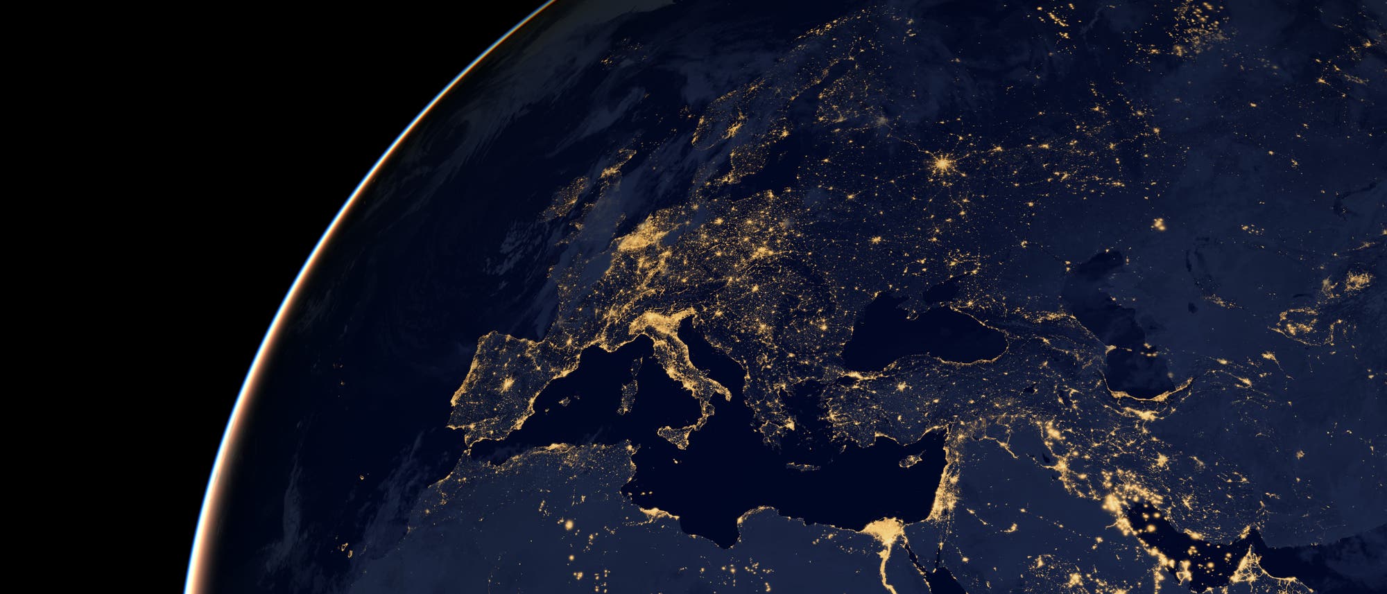 Satellitenbild der Erde bei Nacht, das Europa, Nordafrika und Teile des Nahen Ostens zeigt. Die beleuchteten St&auml;dte und Ballungsr&auml;ume sind deutlich sichtbar und heben sich gegen die dunkle Umgebung ab. Die K&uuml;stenlinien und geografischen Merkmale sind durch die Lichter der St&auml;dte umrissen. Das Bild vermittelt einen Eindruck von Bev&ouml;lkerungsdichte und Urbanisierung in diesen Regionen.