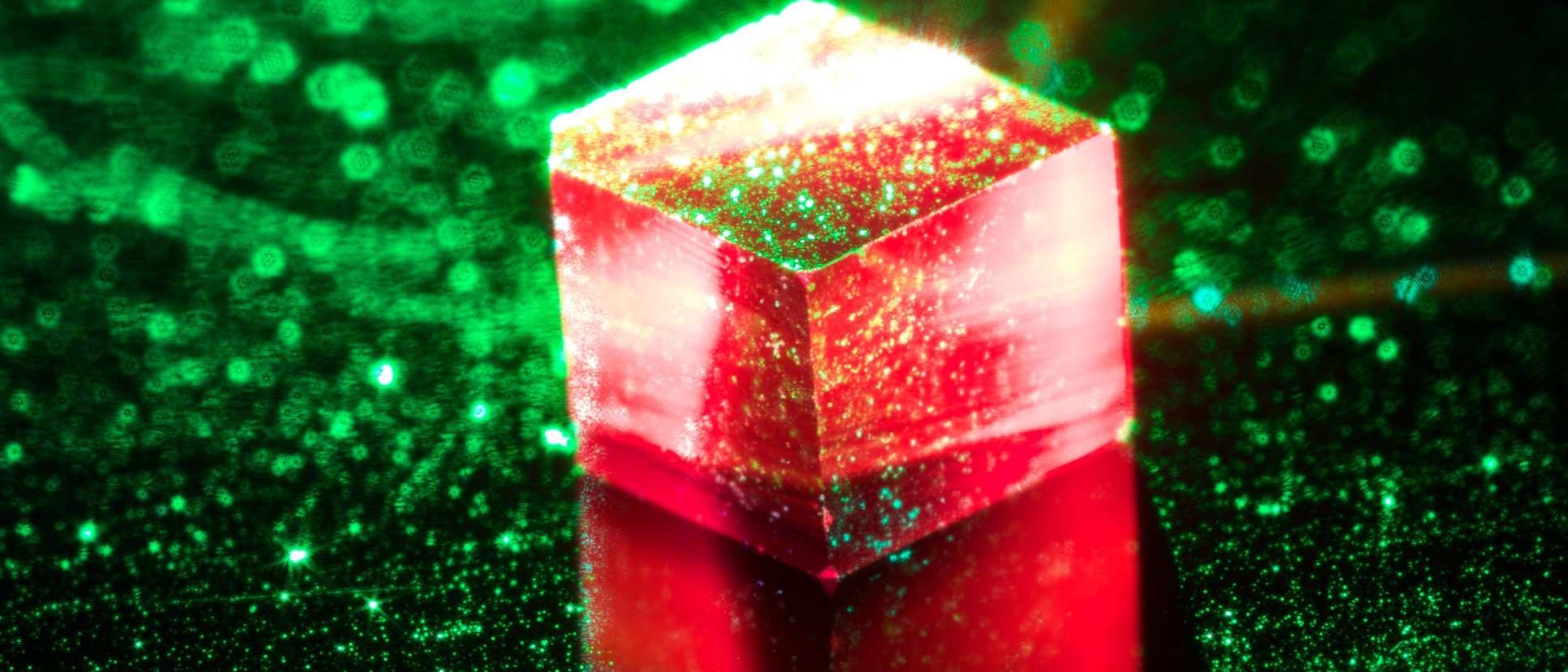 Ein würfelfürmiger Diamantkristall leuchtet rot unter grünem Laserlicht.