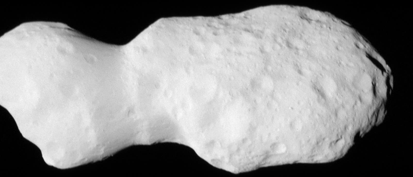 Ein grauer, unregelmäßig geformter Asteroid mit einer rauen, kraterübersäten Oberfläche vor einem schwarzen Hintergrund. Der Asteroid hat eine längliche Form mit einer schmalen Taille in der Mitte. Es sind keine Menschen oder Texte im Bild vorhanden. Ein grauer, unregelmäßig geformter Asteroid mit einer rauen, kraterübersäten Oberfläche vor einem schwarzen Hintergrund. Der Asteroid hat eine längliche Form mit einer schmalen Taille in der Mitte. Es sind keine Menschen oder Texte im Bild vorhanden.