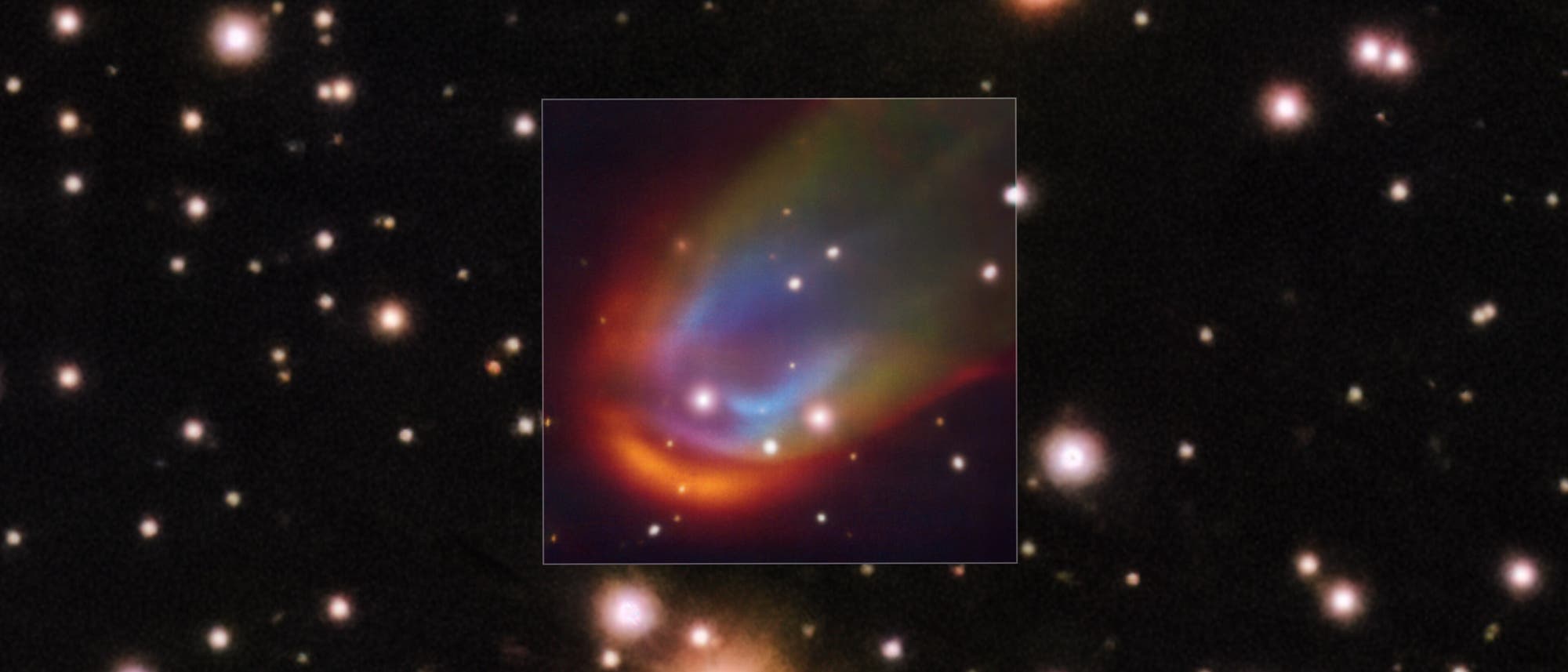 Ein astronomisches Bild zeigt einen Sternenhimmel mit zahlreichen leuchtenden Sternen vor einem dunklen Hintergrund. Im Zentrum befindet sich ein hervorgehobener Bereich mit einem bunten Nebel, der in Rot-, Blau- und Gr&uuml;nt&ouml;nen leuchtet. Der Nebel umgibt mehrere helle Sterne und bildet eine geschwungene, wolkenartige Struktur. Das Bild vermittelt die Weite und Sch&ouml;nheit des Universums und hebt die faszinierenden Farben und Formen kosmischer Ph&auml;nomene hervor.