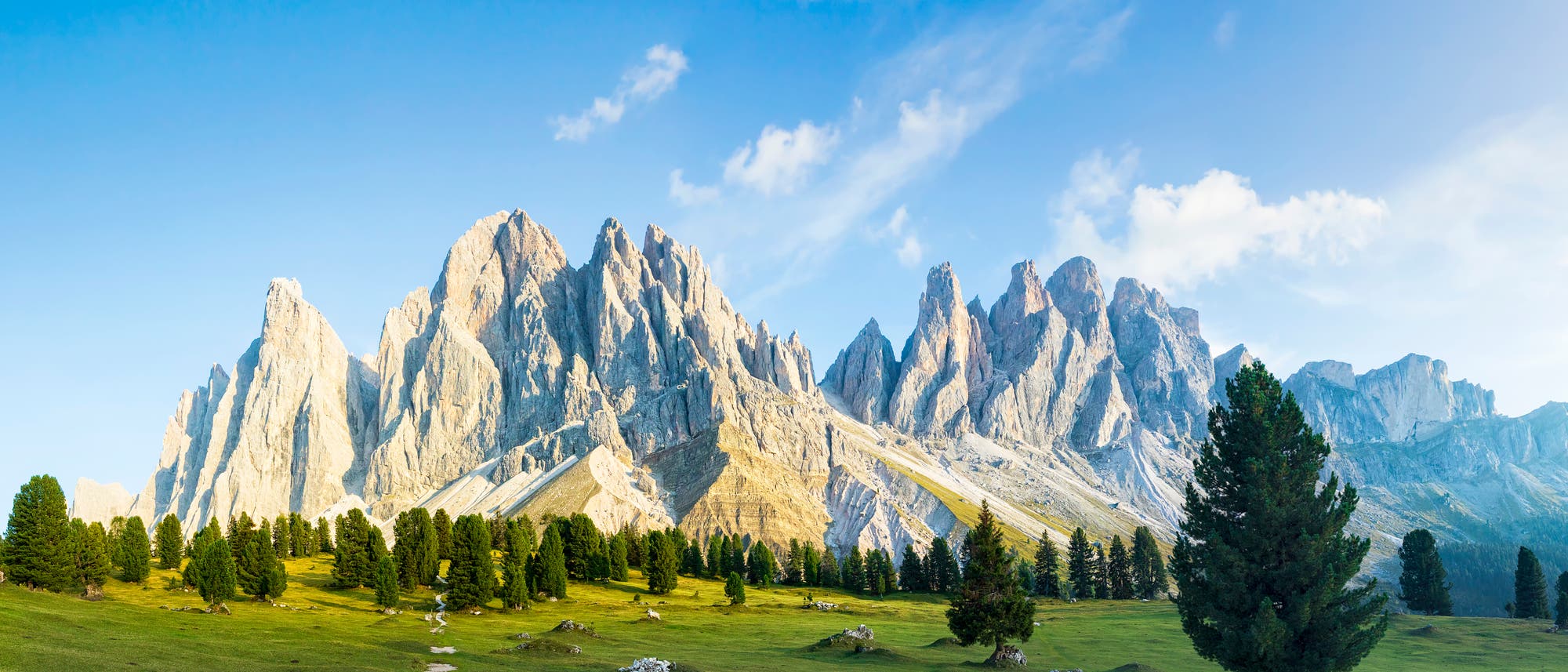 Steile Felszacken aus hellem Gestein über grüner Wiesenlandschaft, Geisler Gruppe in den Dolomiten.