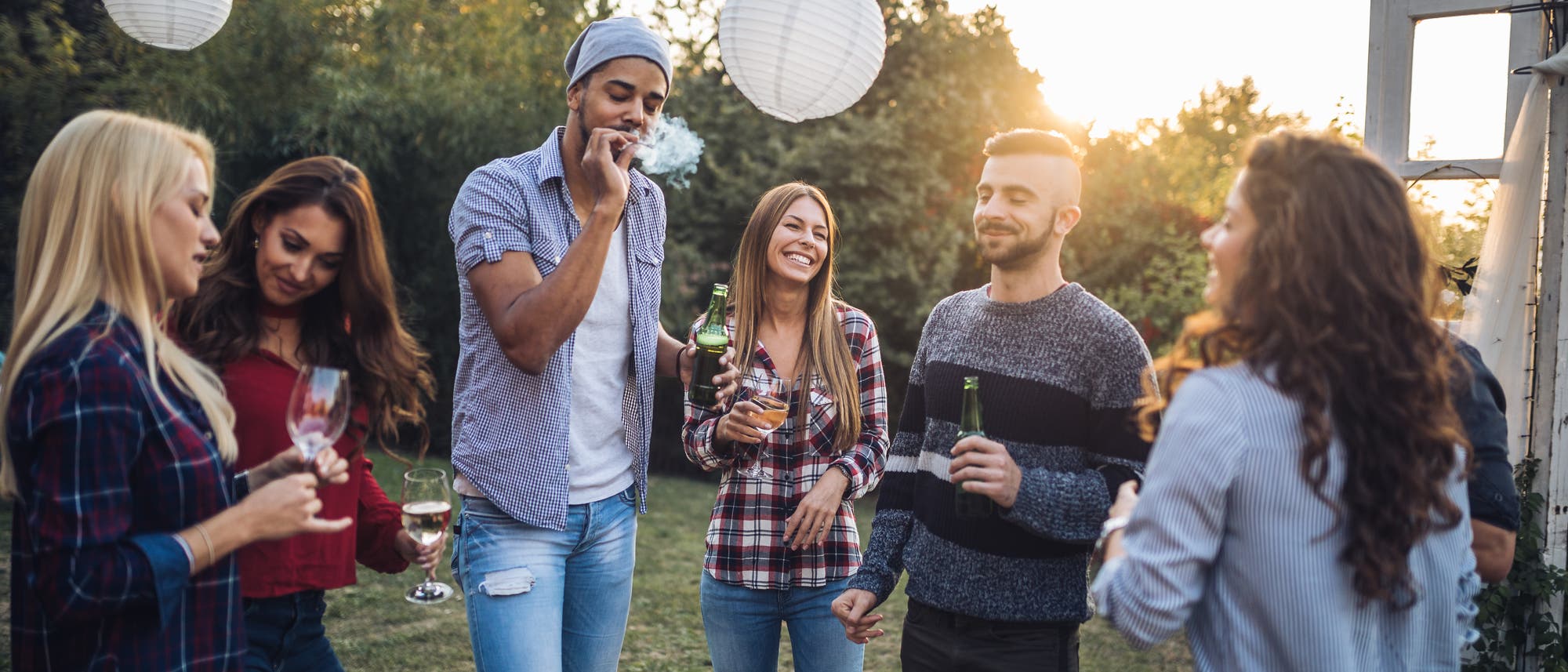 Eine Gruppe junger Menschen sind in einem Garten und haben Spaß beim Rauchen und Trinken