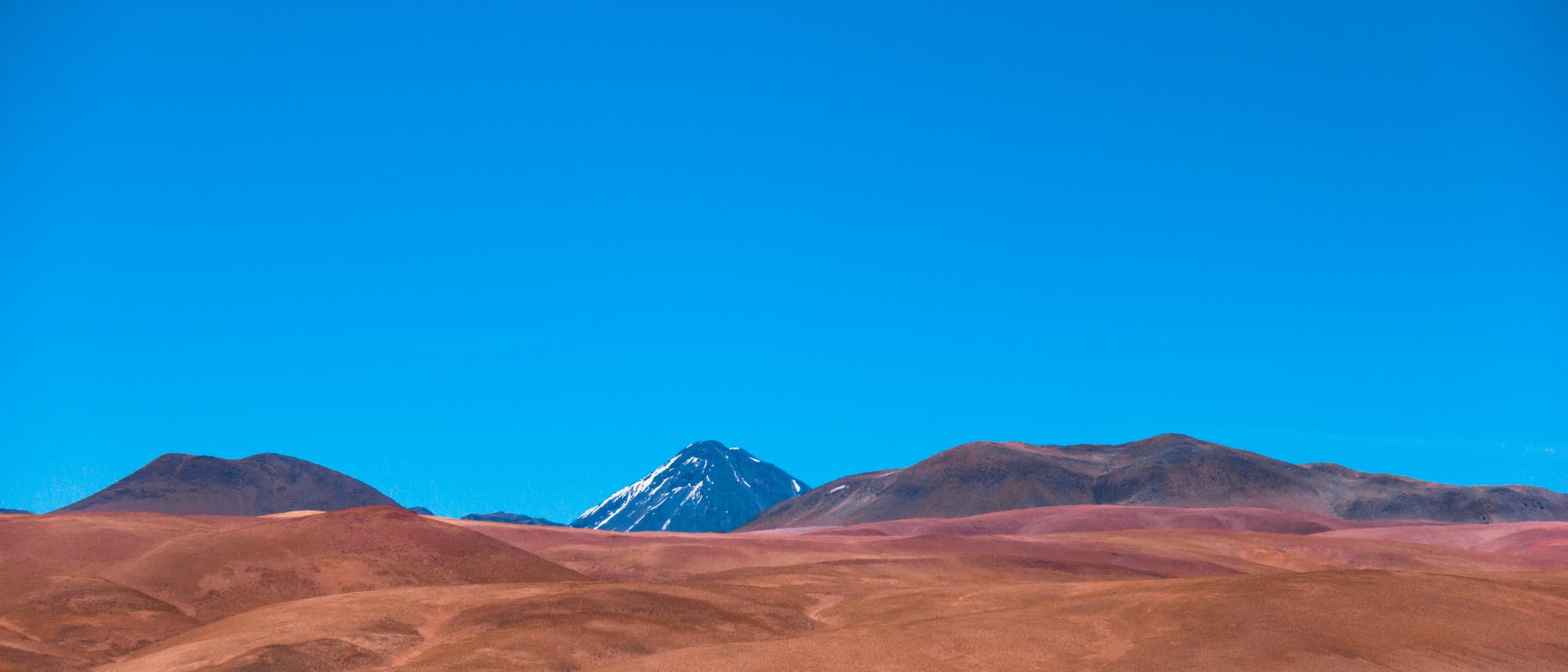 Altiplano in Chile: Ein Vulkan ragt unter einem stahlblauen Himmel über der Wüste auf.