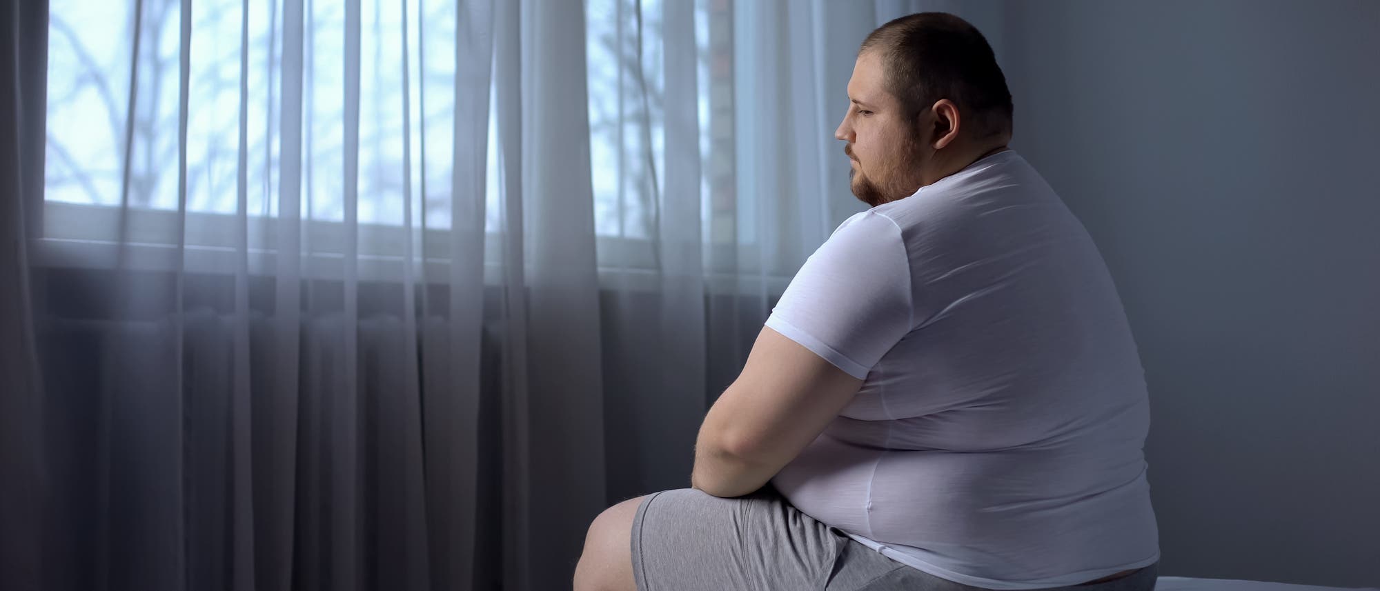 Übergewichtiger Mann sitzt auf Bettkante