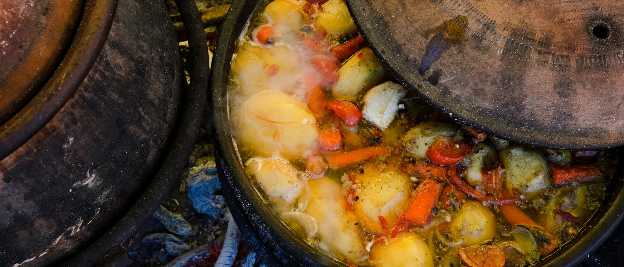 In einem modernen Tontopf kocht ein Gemüsegericht, erhitzt auf glühenden Kohlen. 