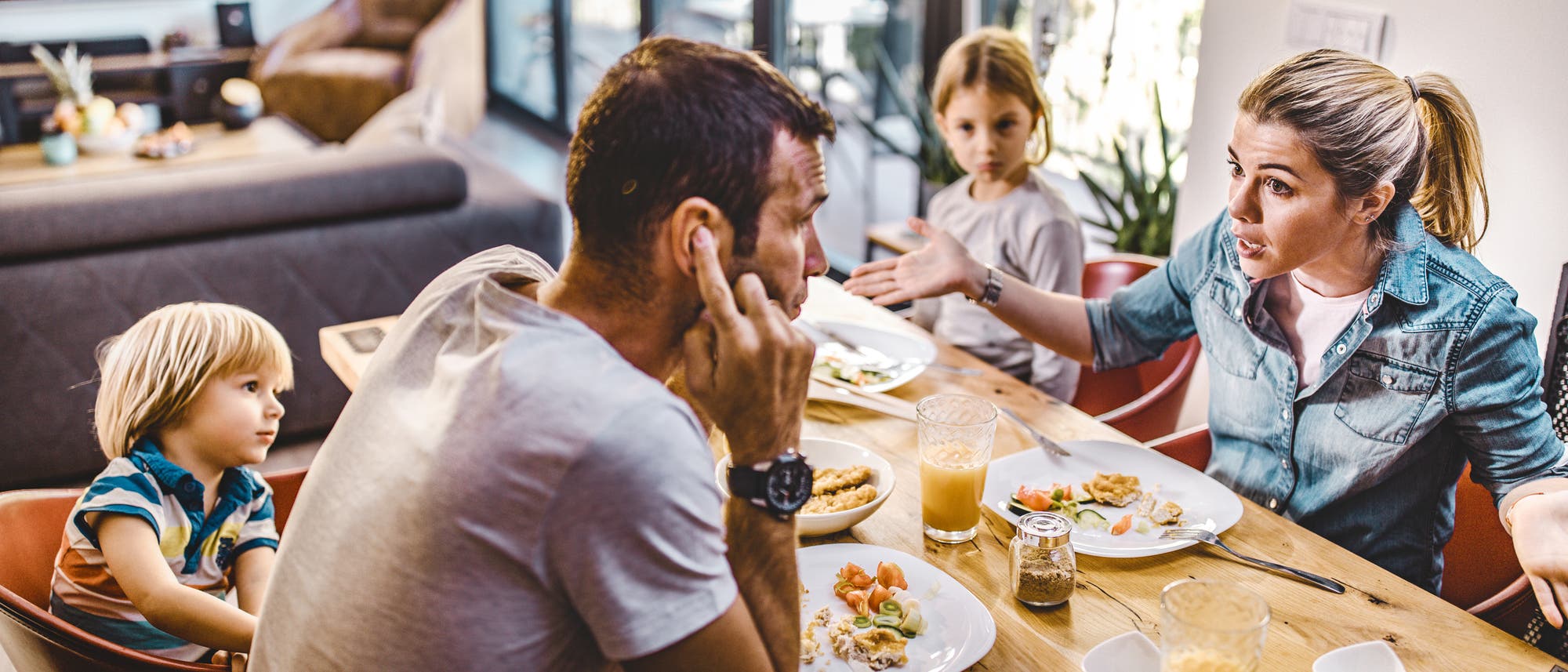 Eine Familie sitzt gemeinsam beim Essen am Tisch. Die Mutter meckert, der Vater h&auml;lt sich die Ohren zu, und die Kinder schauen best&uuml;rzt.