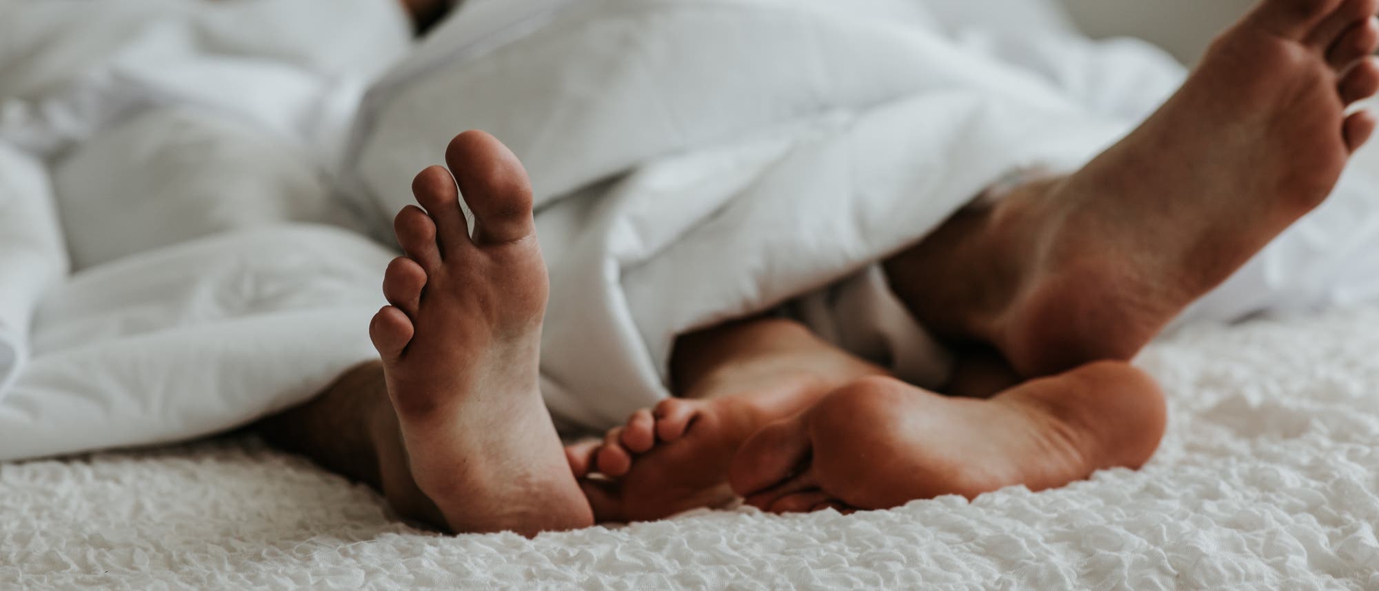 Füße eines Paares unter einer Bettdecke