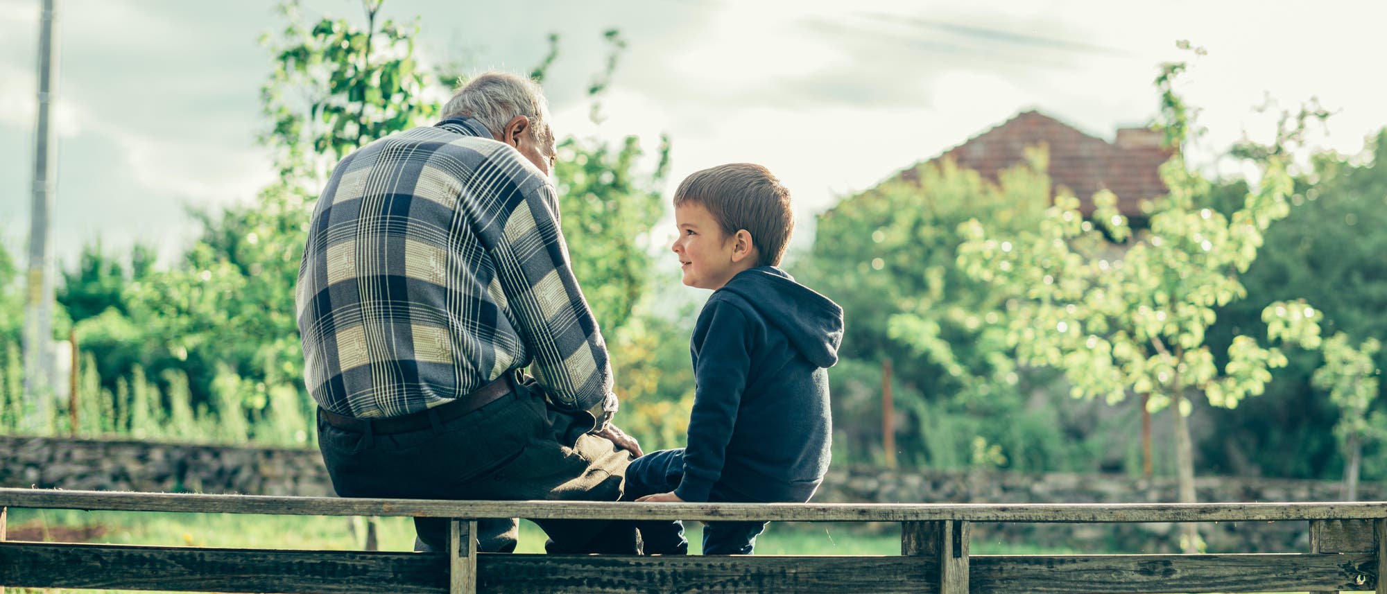 Kleiner Junge und alter Mann sitzen auf einem Zaun und sprechen miteinander