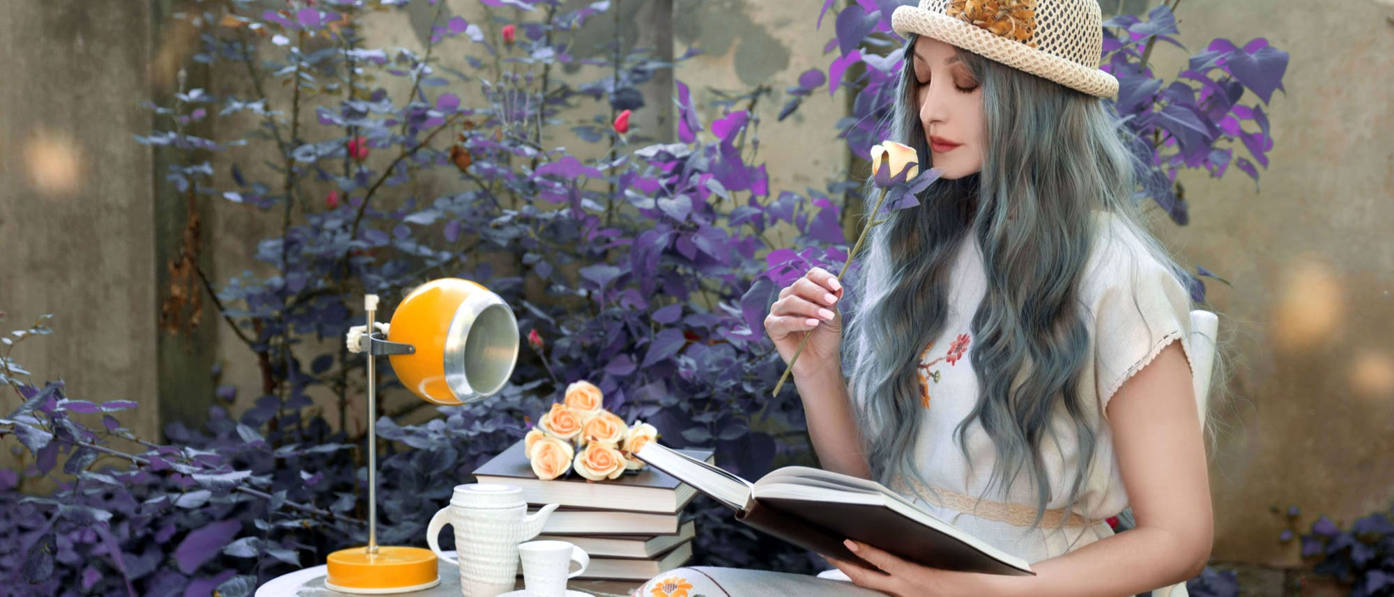 Frau riecht an einer Rose, während sie im Garten in einem Buch liest