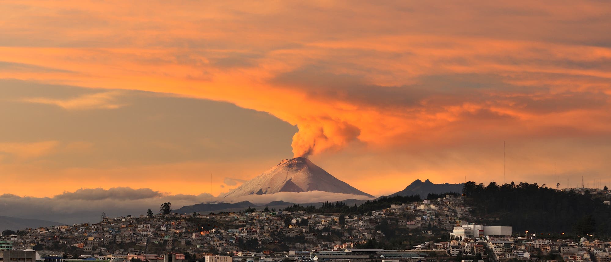 Ausbruch des Vulkans Cotopaxi nahe der Stadt Quito. Im Vordergrund das Stadtzentrum, im Hintergrund ein rauchender Vulkankegel.