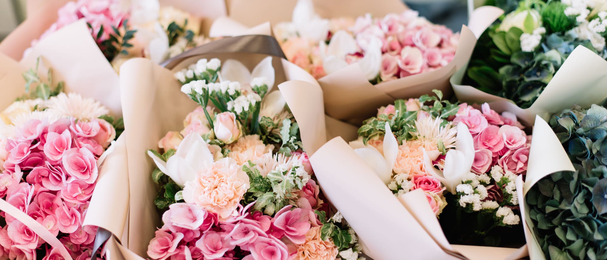 Auf einem Tisch liegen mehrere bunte Sträuße mit Hortrensien, Rosen, Pfingstrosen und anderen Blumen.