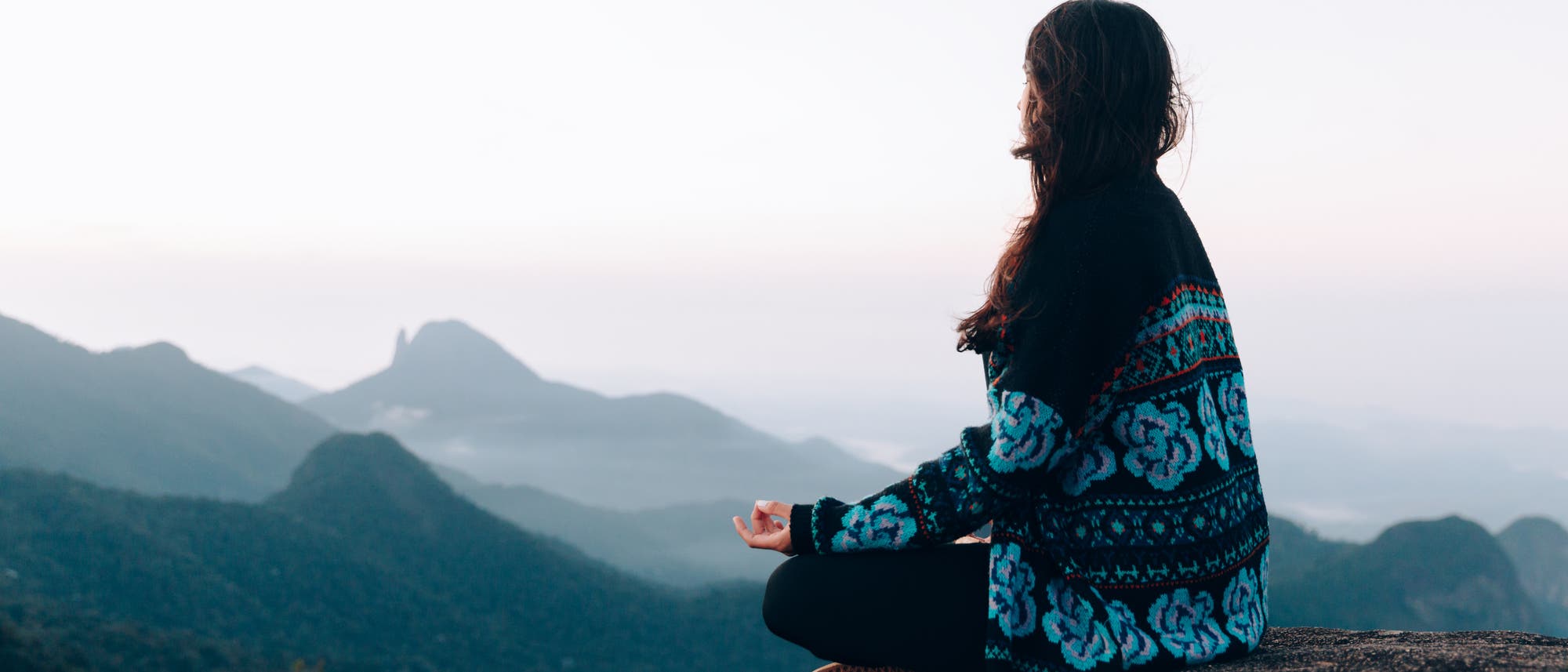Eine Frau meditiert auf einem Gipfel mit Blick über die Berge