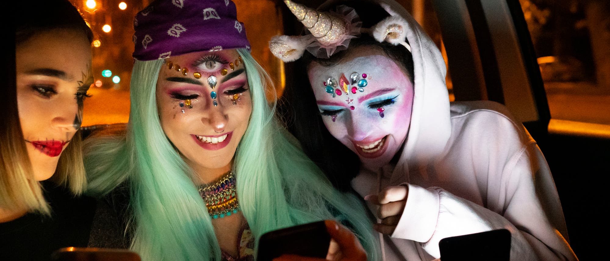 Zwei junge Frauen und ein Einhorn kommunizieren auf dem Weg zum Kostümball mit sich und ihren Smartphones