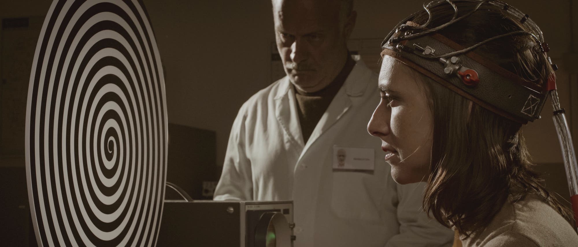 Frau mit Kabeln am Kopf schaut auf eine Spirale, beobachtet von einem Forscher
