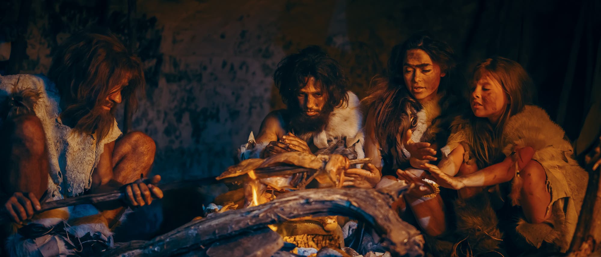Prähistorische Jäger und Sammler tragen Tierhäute und essen Fleisch in einer Höhle in der Nacht