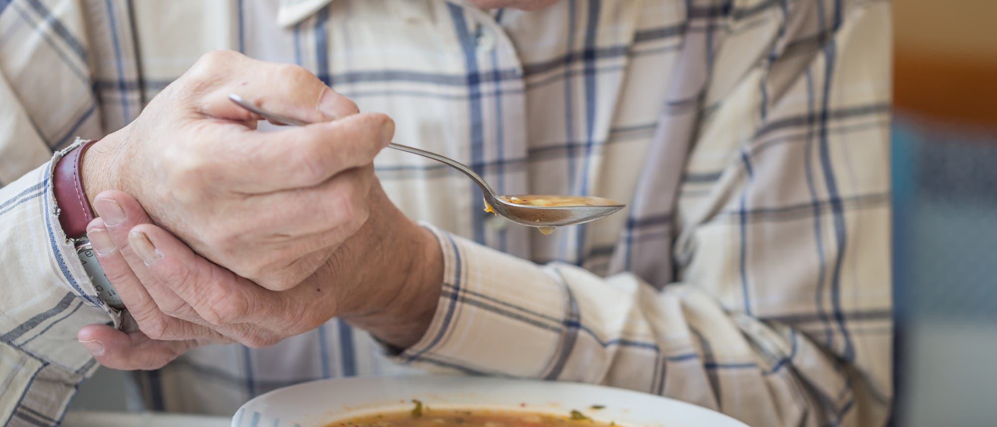 Alter Mann stützt seine Hand um seine Suppe auslöffeln zu können.