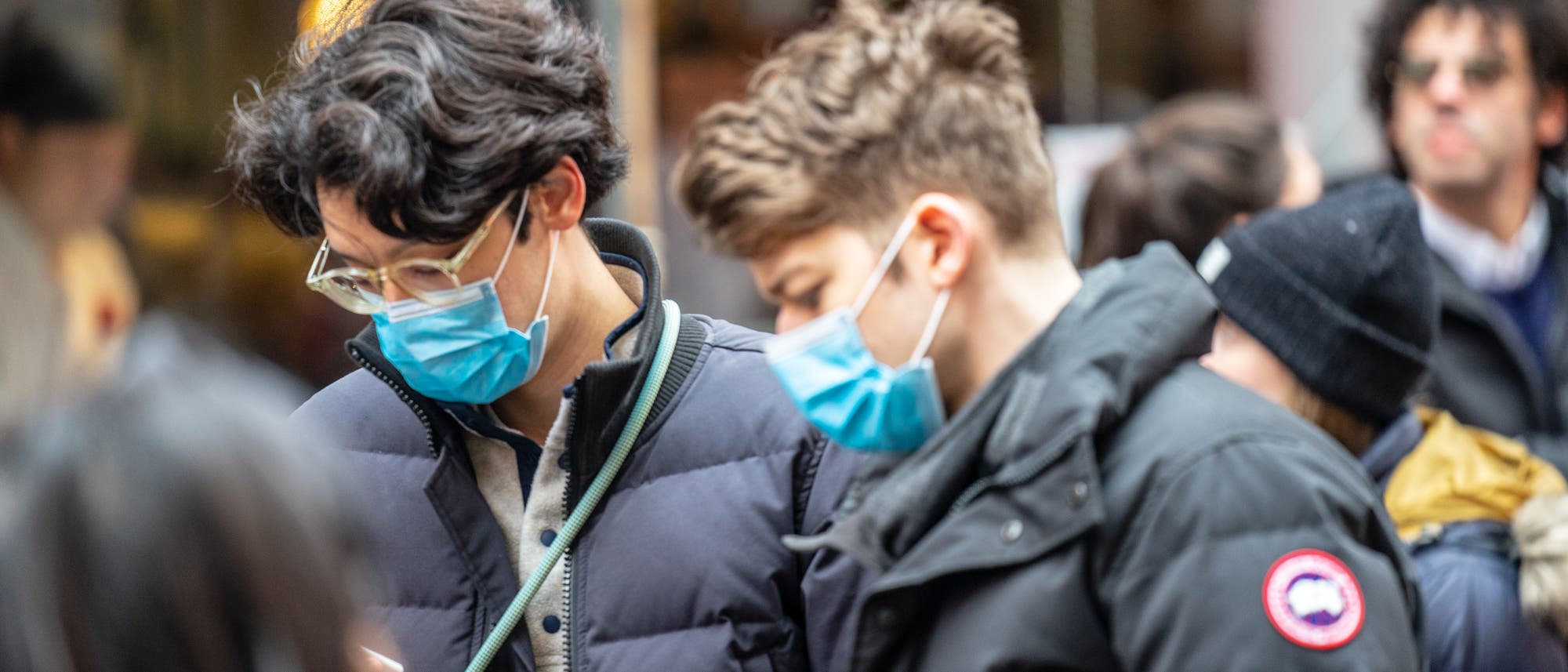 Zwei Junge Männer mit Mundschutz gucken auf ihre Handys, um den neuesten Spektrum-Artikel über das Coronavirus zu lesen.