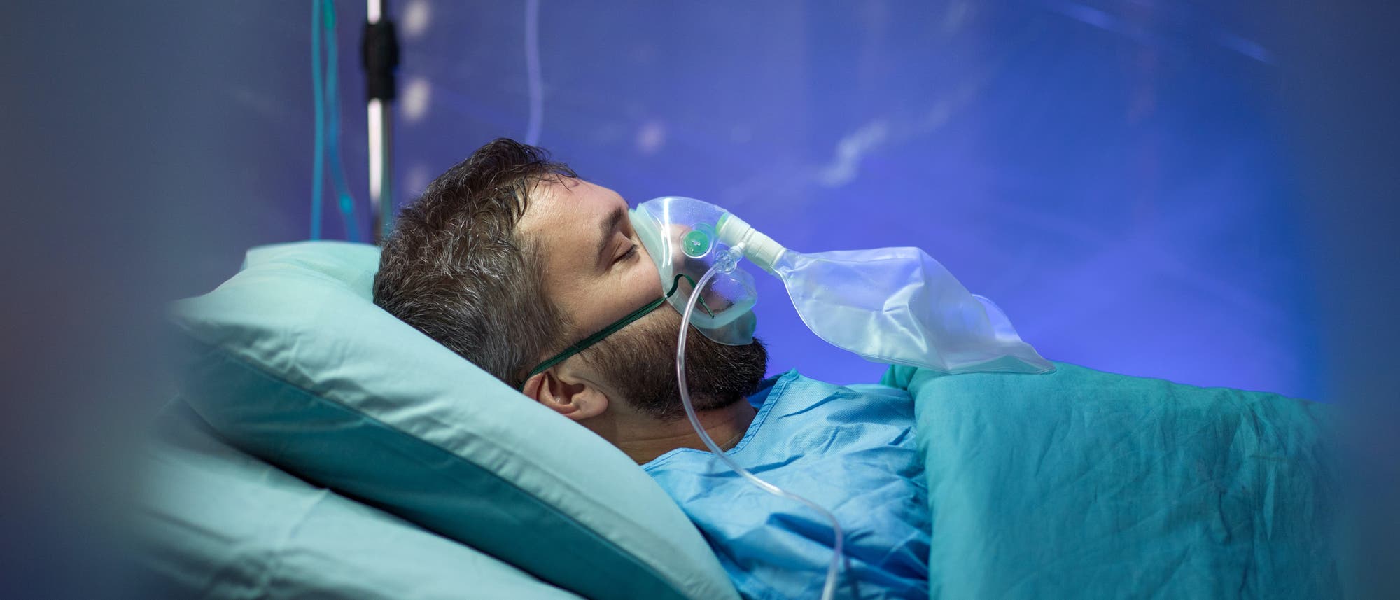 Ein junger Mann mit Beatmungsgerät liegt in einem Krankenhausbett.