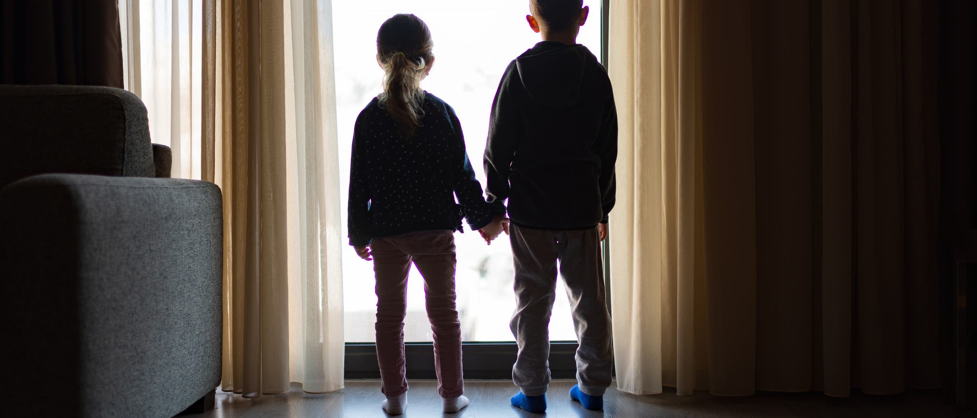 Mädchen und Junge im Gegenlicht vor einer gläsernen Tür