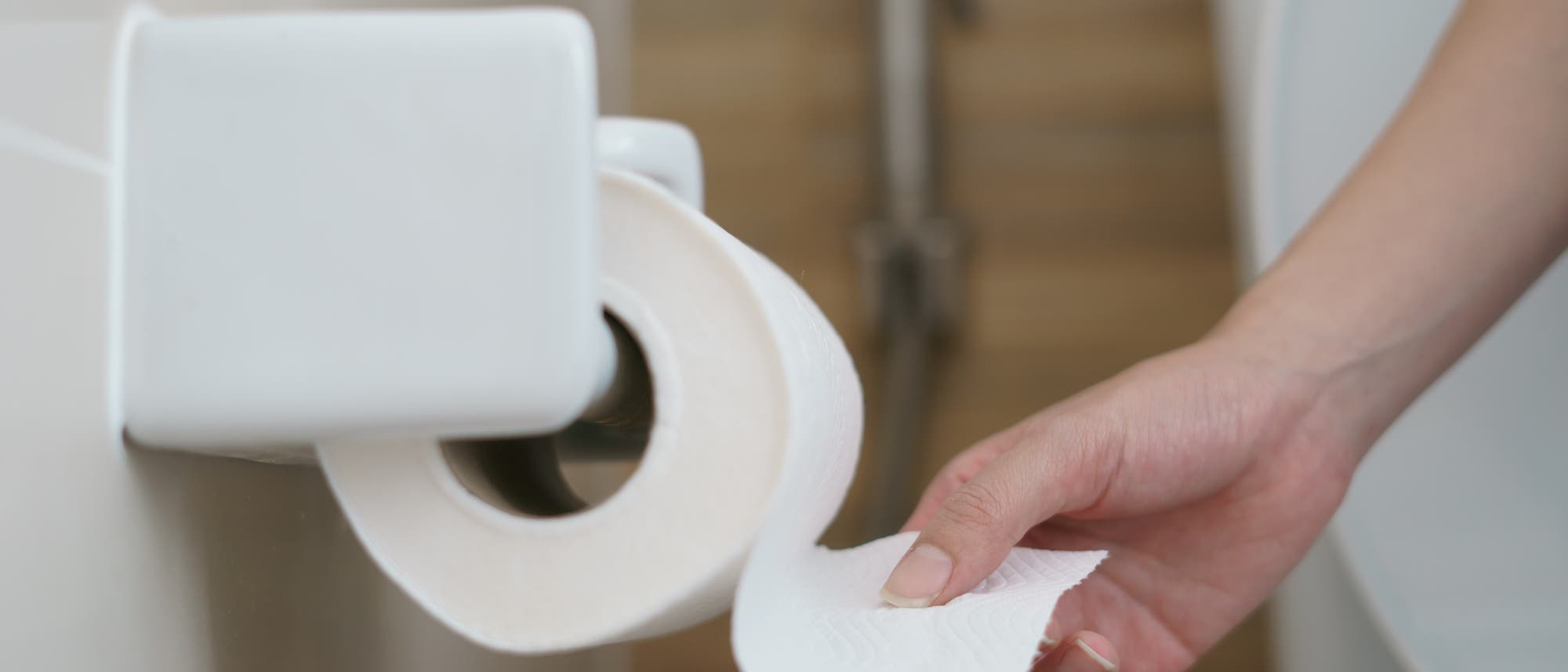 Eine Hand reißt ein Blatt von einer Klopapierrolle ab Eine Hand reißt ein Blatt von einer Klopapierrolle ab