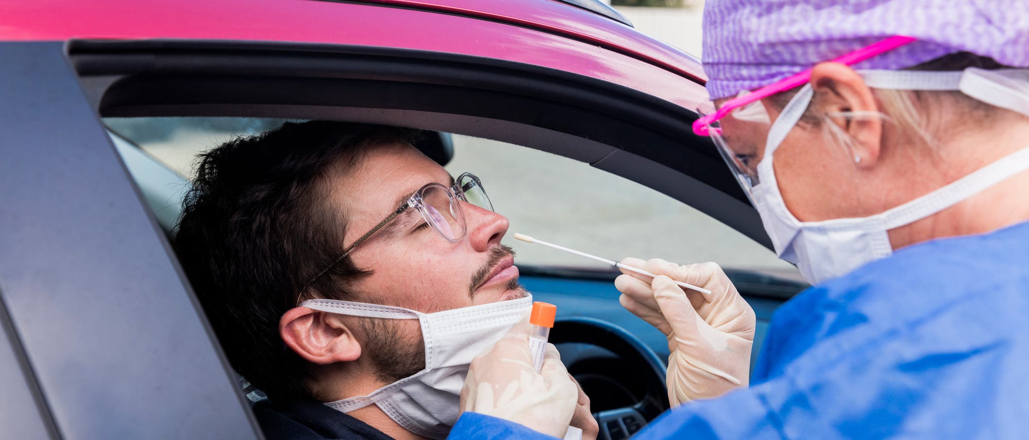 Ein Mediziner in Schutzkleidung nimmt einen Nasenabstrich von einem Autofahrer.
