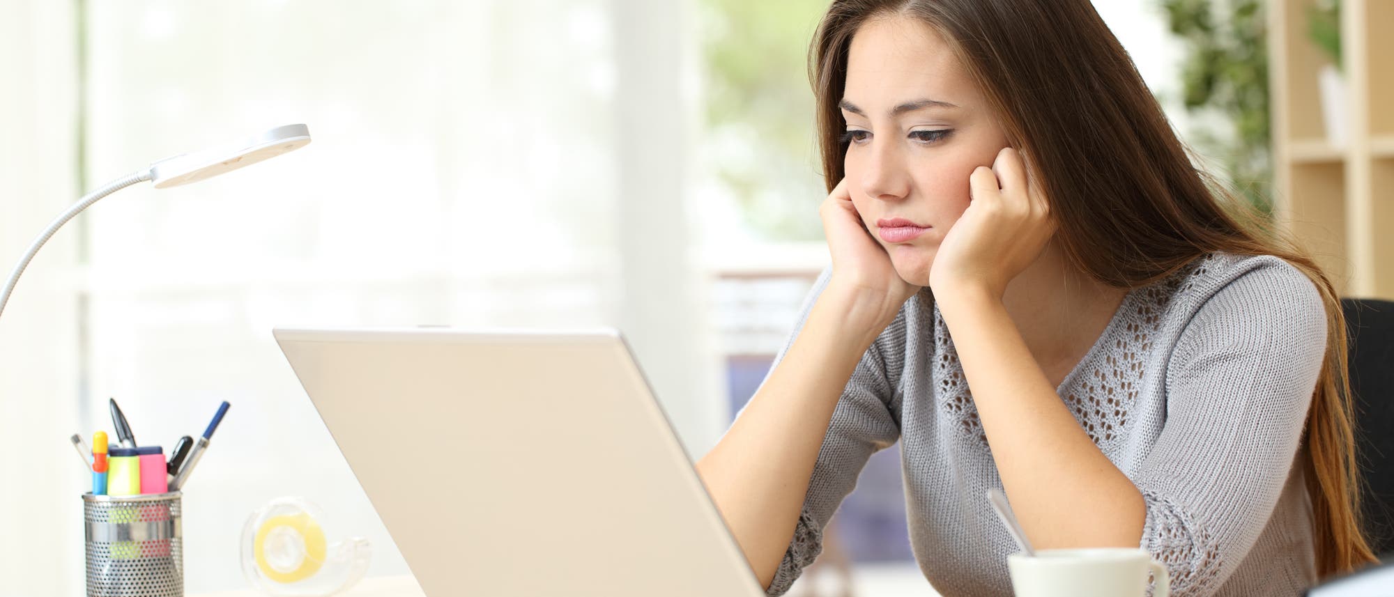 Eine Frau sitzt vor ihrem Laptop, mit traurigem Gesichtsausdruck.
