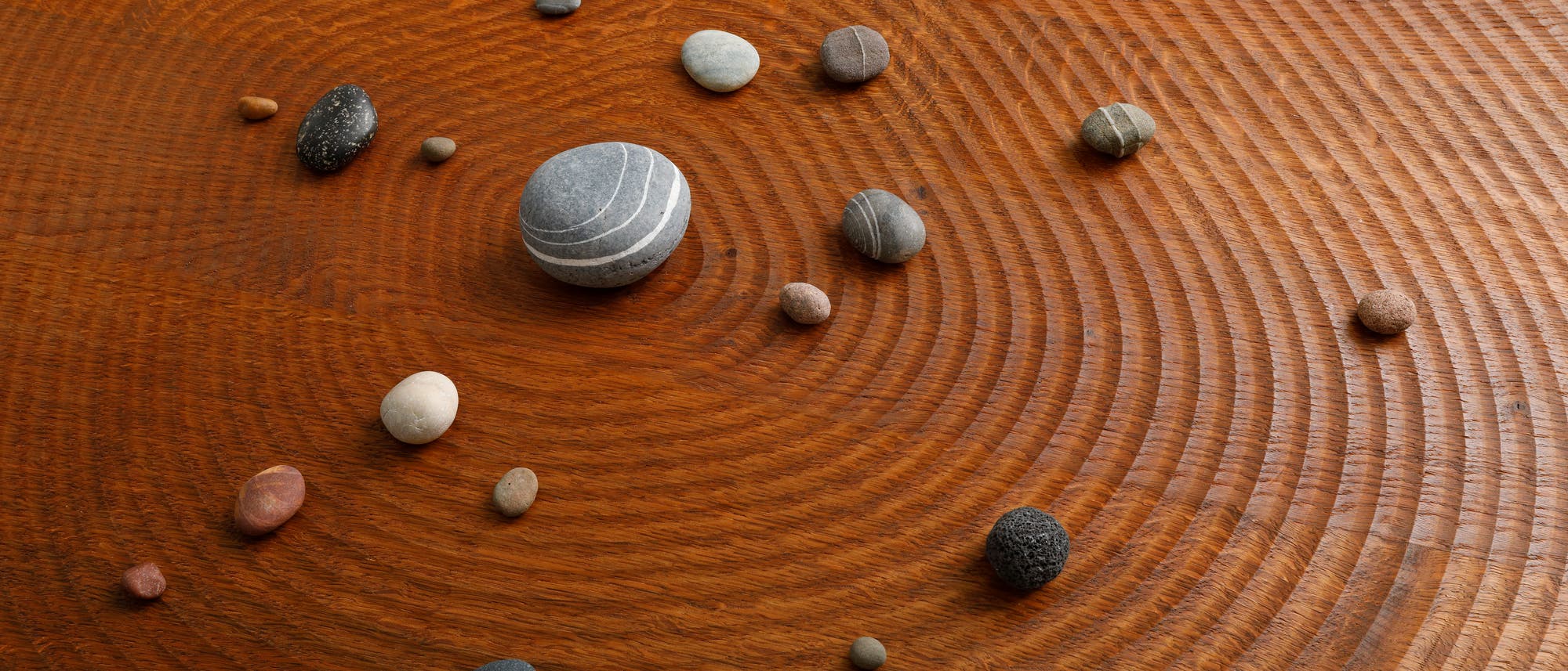Eine mit elliptischen Einkerbungen geriffelte Holzplatte, auf der diverse mittelhübsche Steine angeordnet sind.