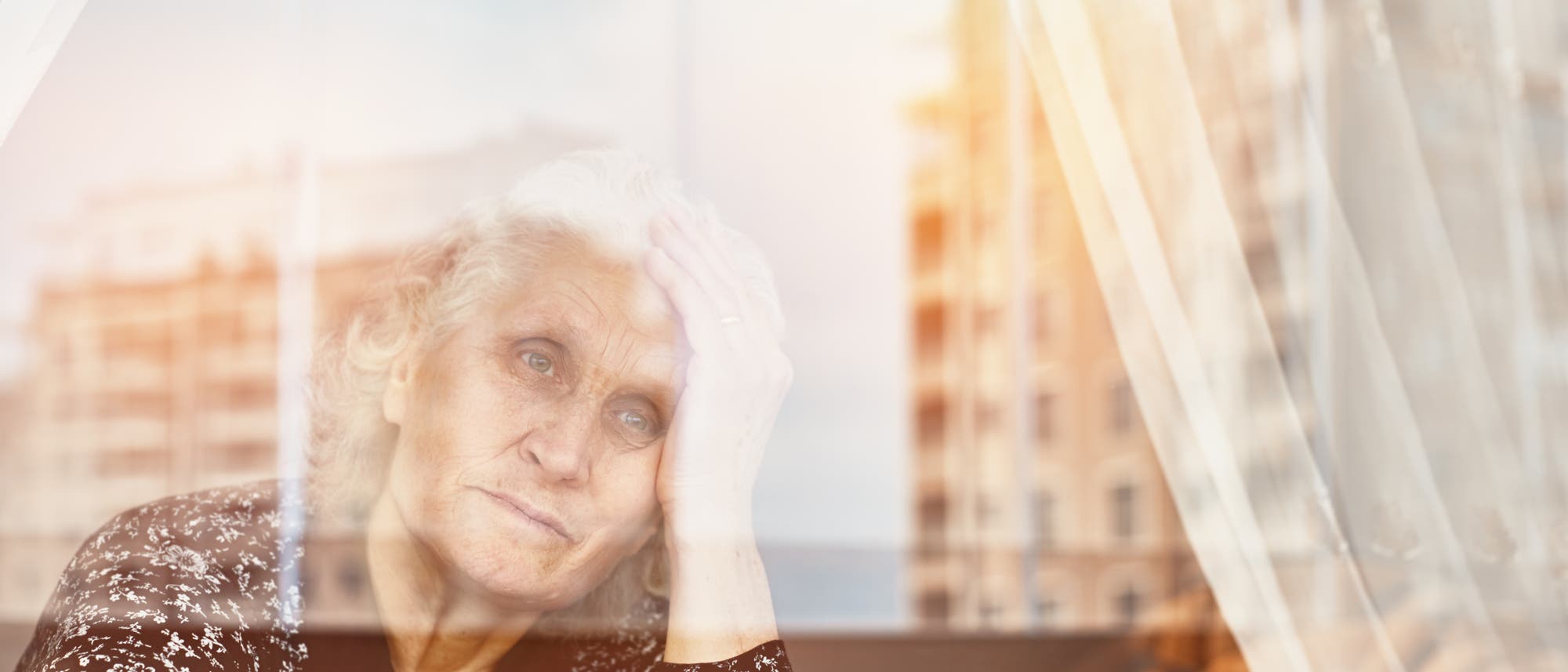 Eine ältere Frau schaut traurig aus ihrem Fenster. Die Farben sind blass.