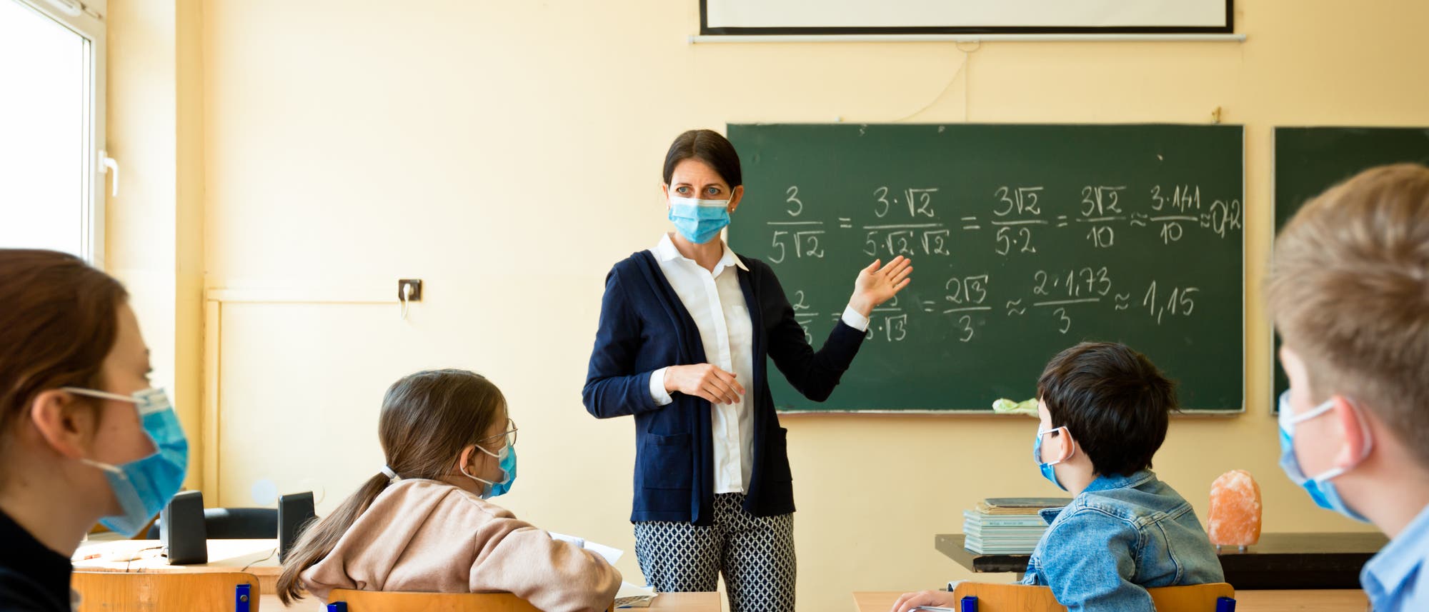 Lehrerin und ihre Klasse mit Masken im Klassenraum