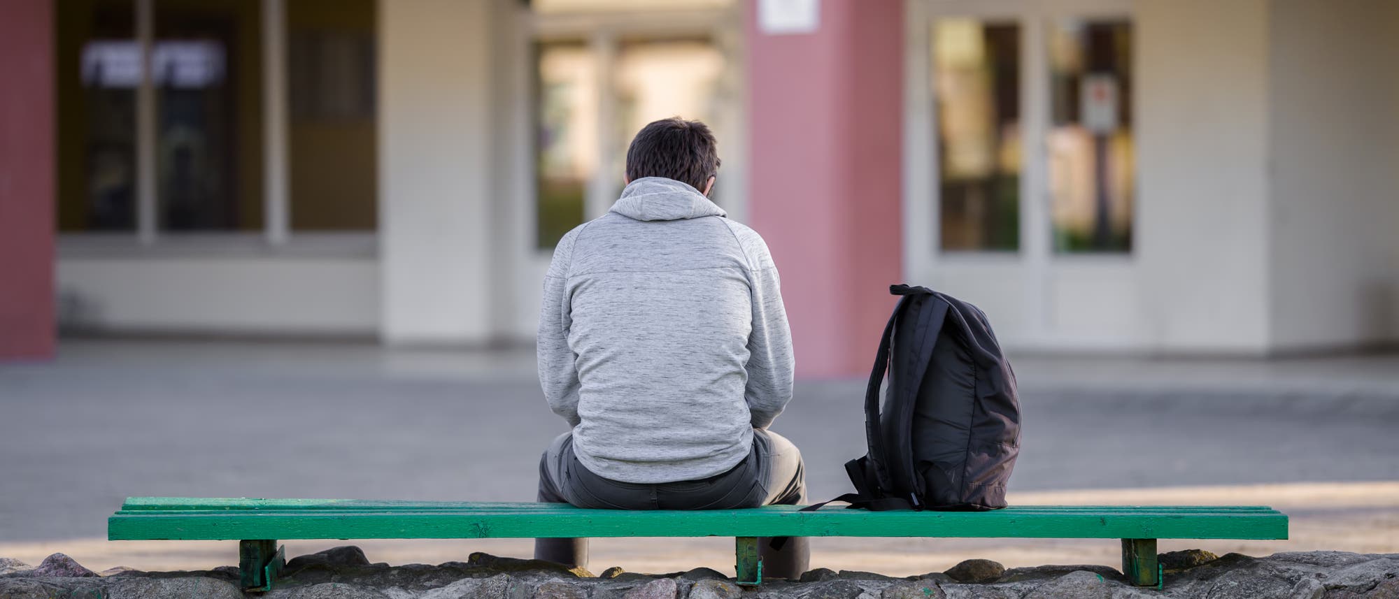 Ein Jugendlicher sitzt auf einer Bank auf dem Schulhof. (Symbolbild)