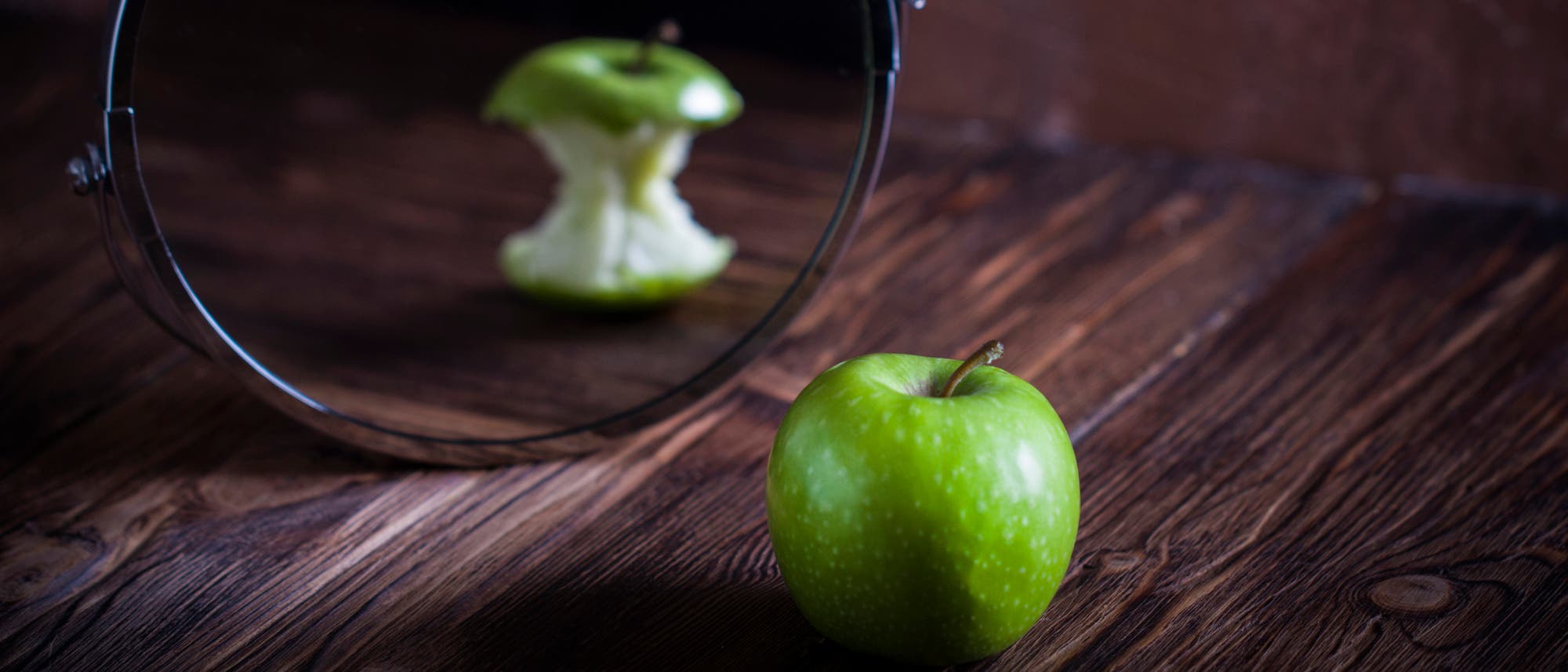 Ein vollständiger grüner Apfel erscheint im Spiegel als abgenagter Apfel