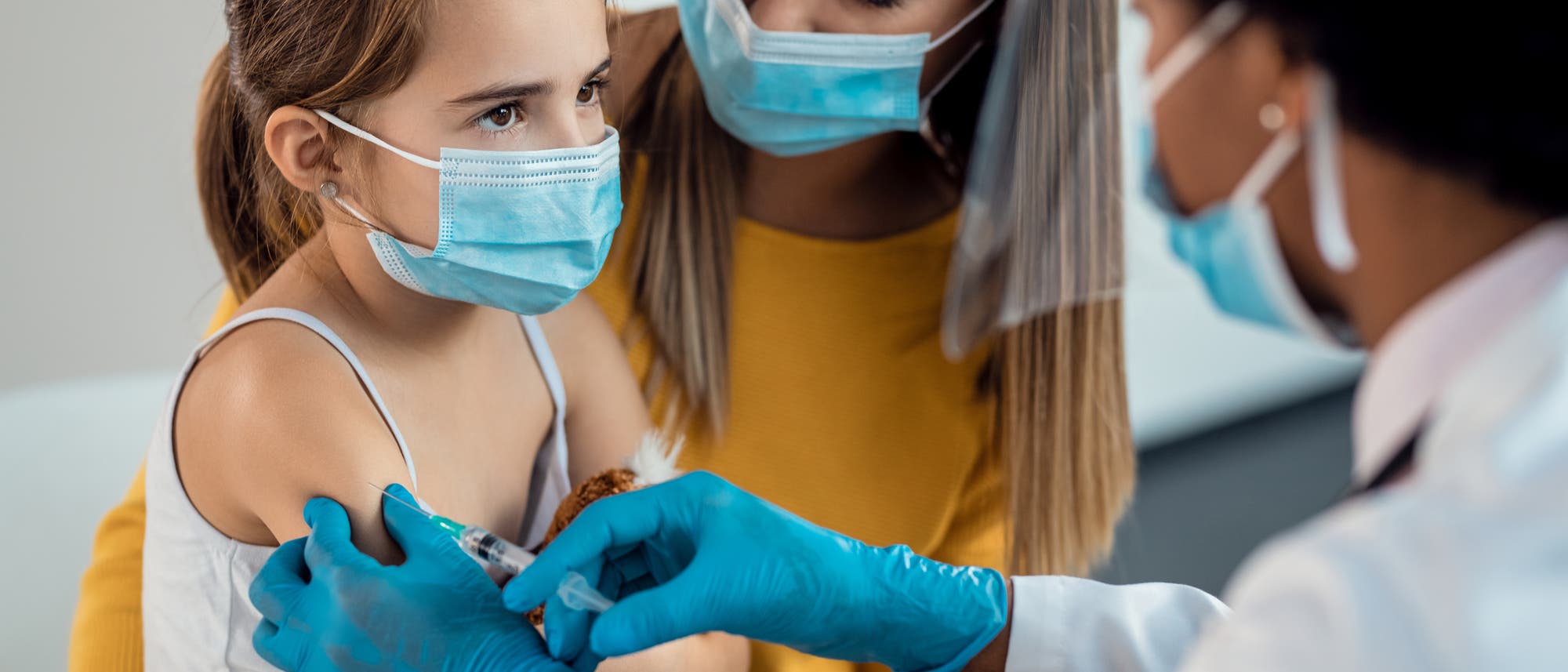 Ein Kind mit Maske wird von einer Ärztin geimpft