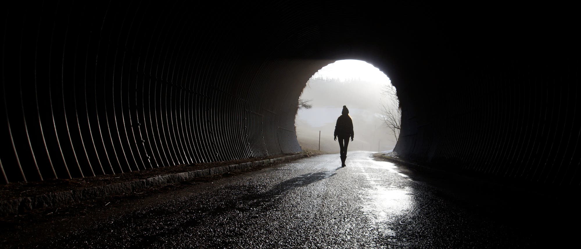 Die Silhouette einer Frau, die sich dem Ende eines dunklen Tunnels nähert