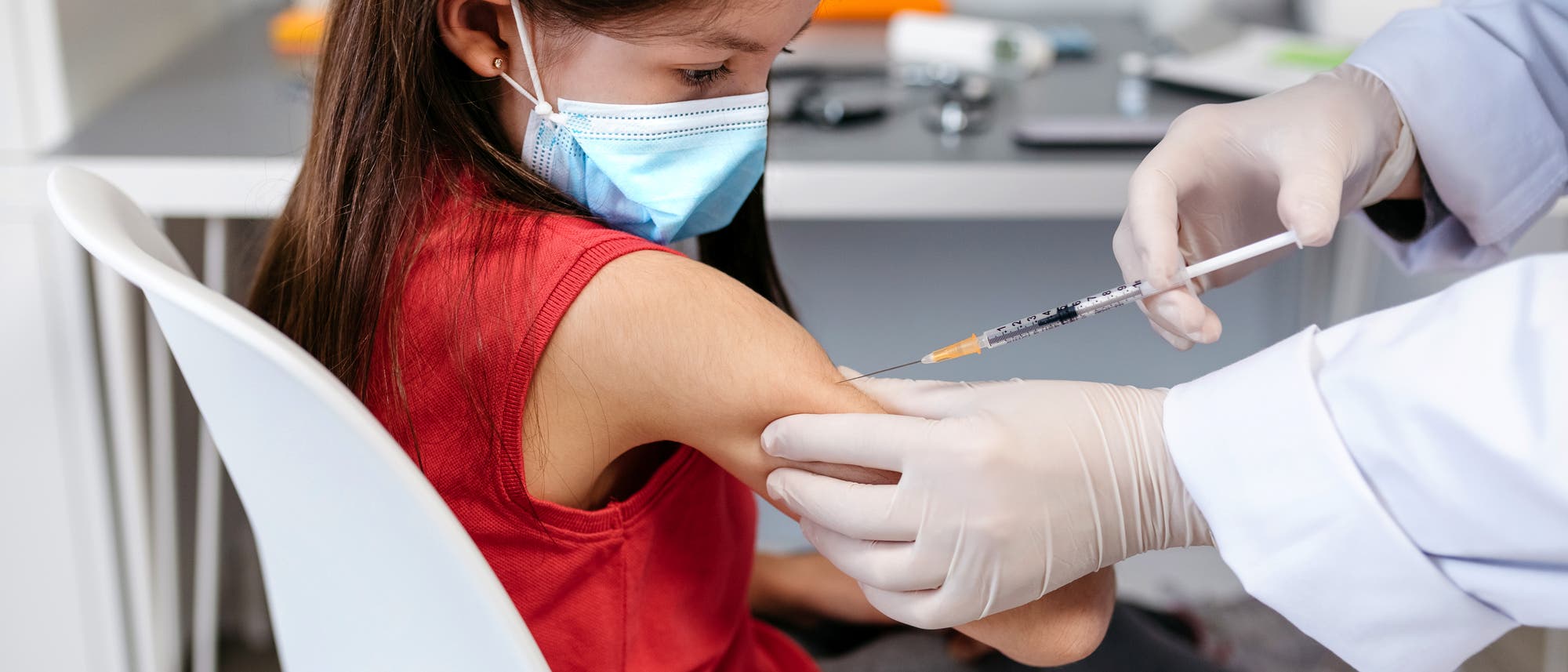 Ein Kind im roten Shirt bekommt eine Impfung in den Oberarm.