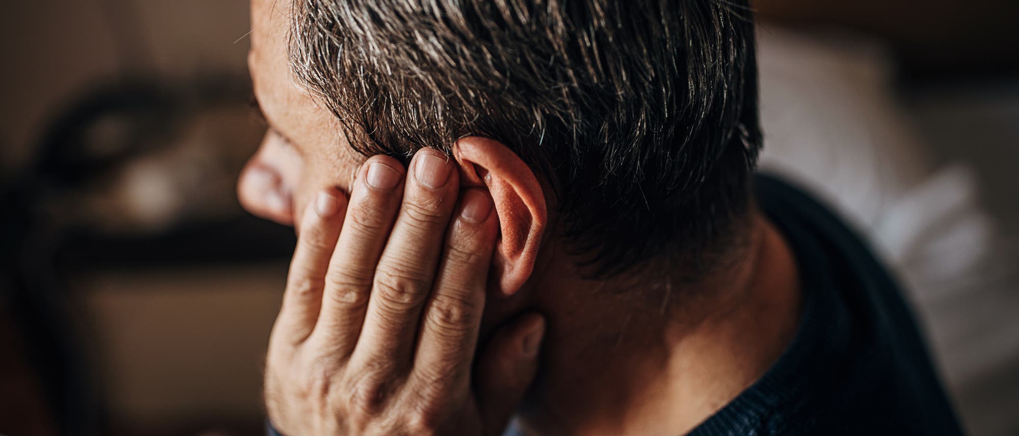 Ein Mann hält sich wegen Schmerzen das Ohr zu.